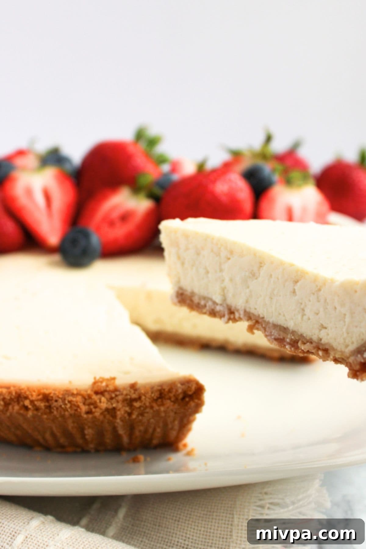 A hand reaching for a slice of Greek yogurt cheesecake from a plate, beautifully garnished.