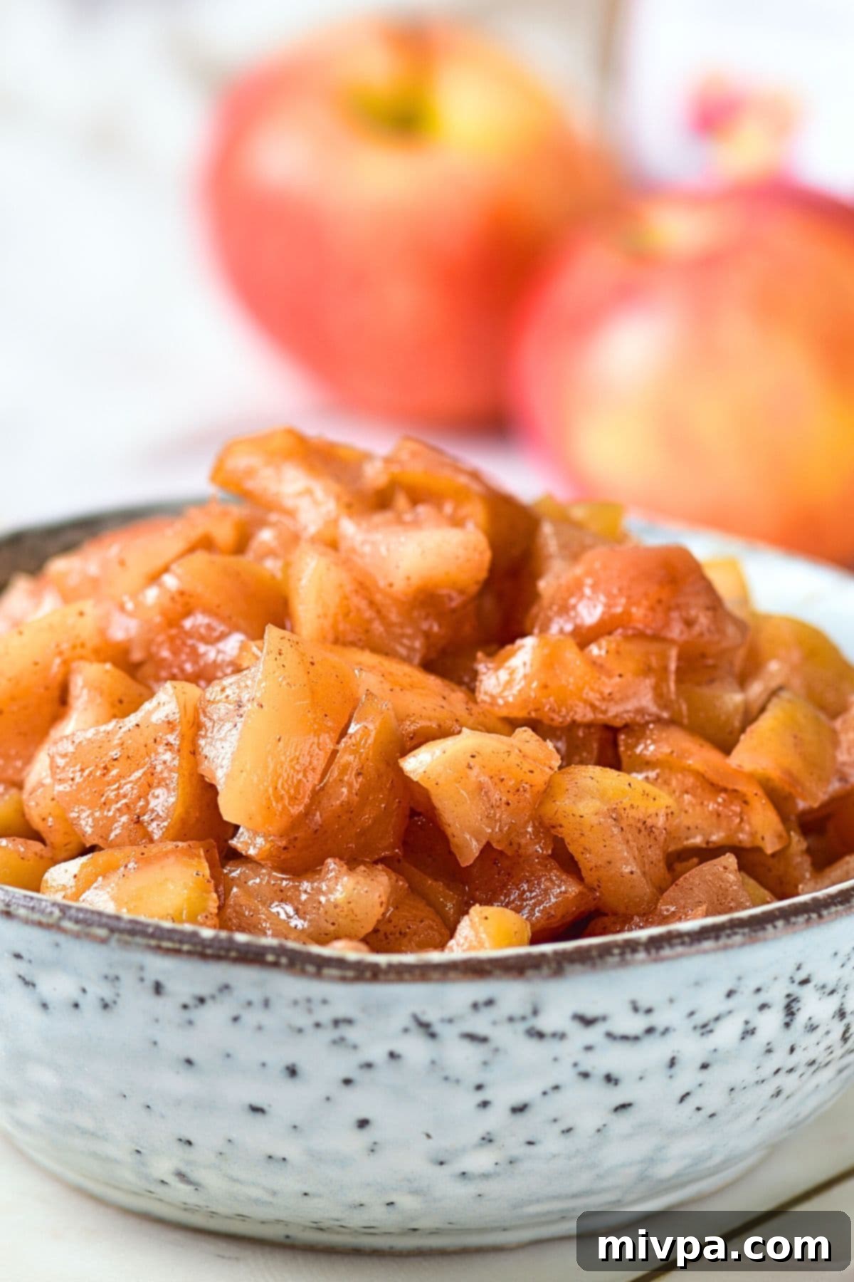 Caramelized Apples (Gluten-Free, Vegan) A bowl of caramelized apples with two apples in the background
