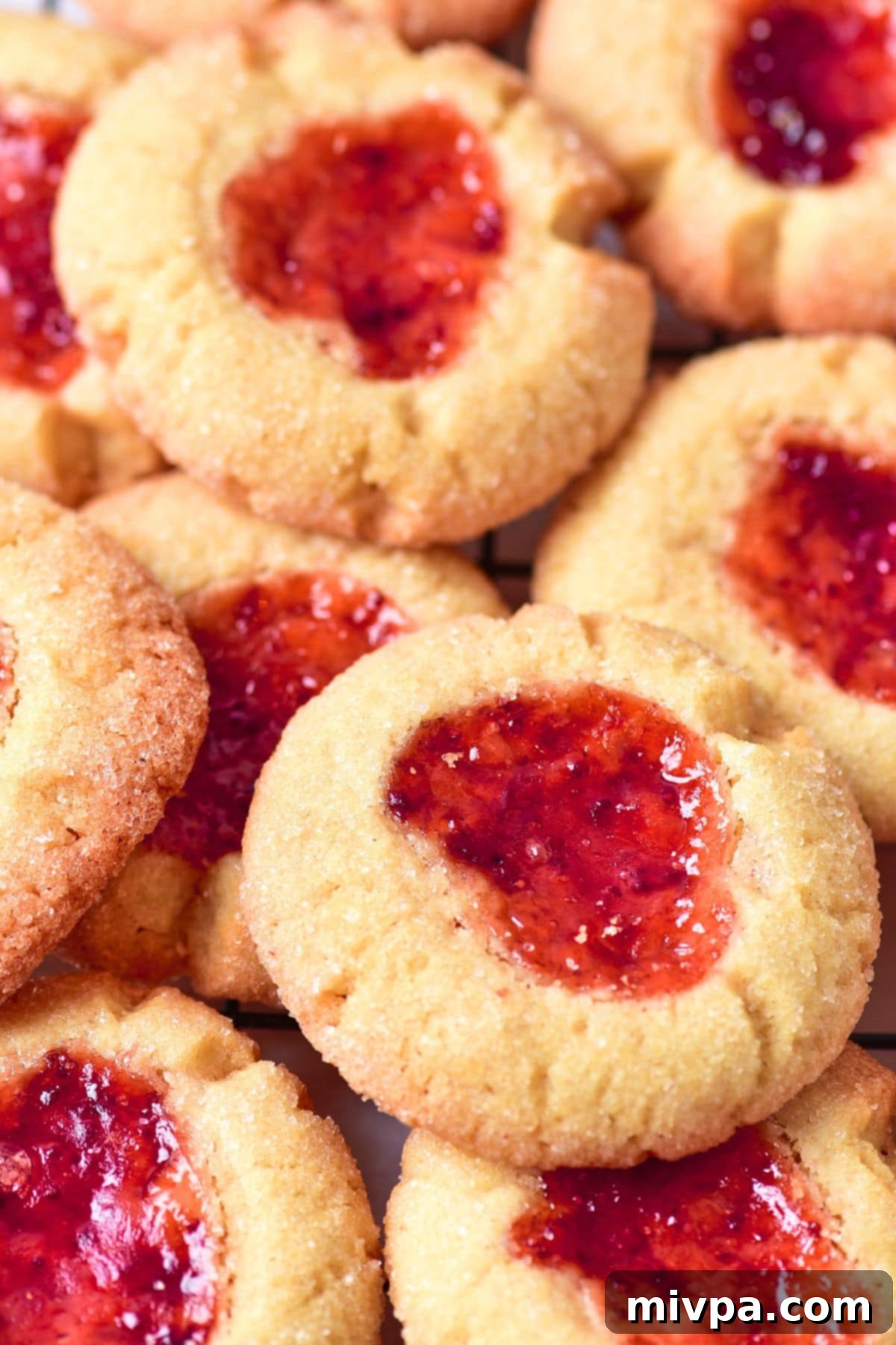 Gluten-Free Thumbprint Cookies (Dairy-Free) Up close view of gluten-free thumbprint cookies filled with red jam and rolled in sugar.
