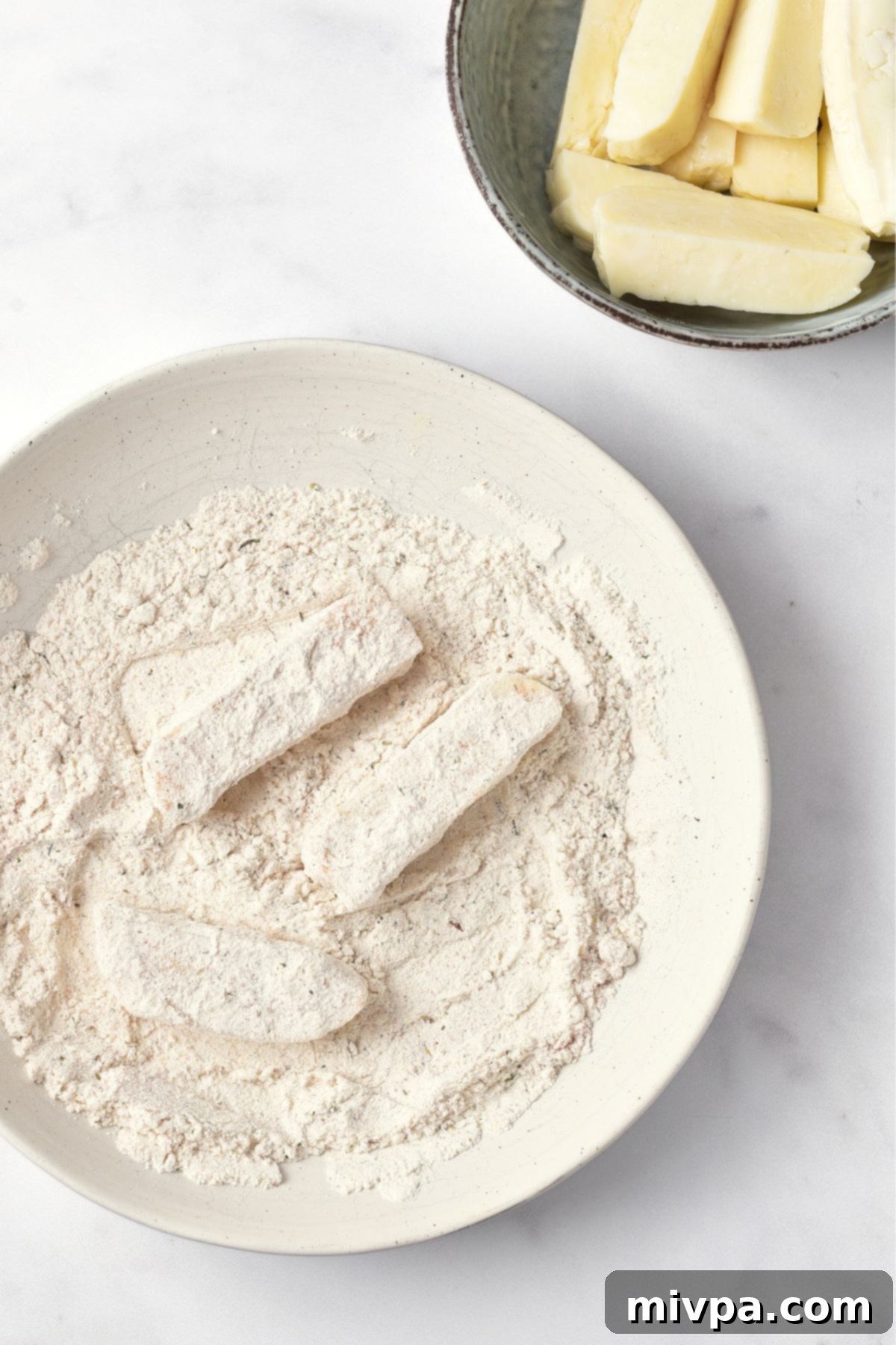Halloumi cheese strips being coated in a dry flour and spice mixture in a bowl, ensuring an even layer.