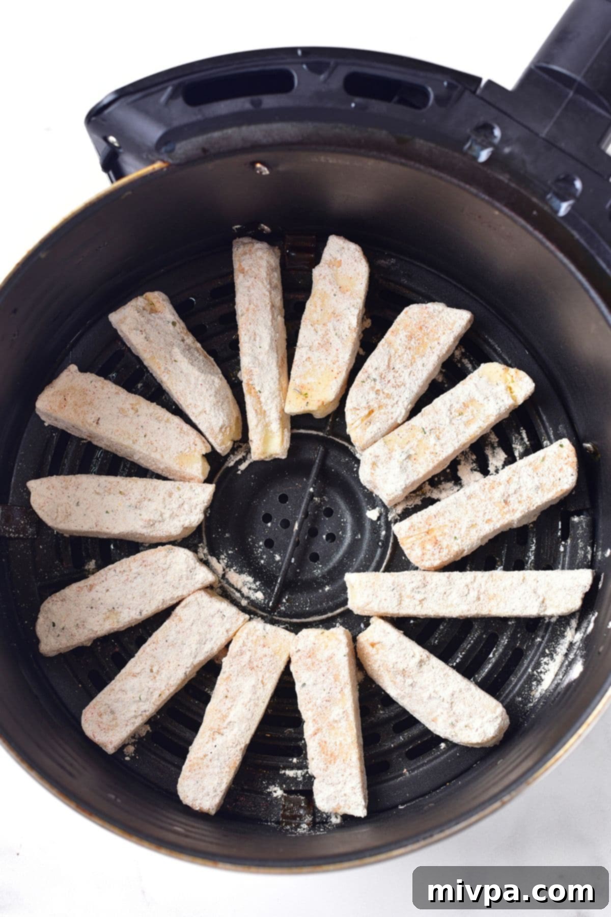 Flour-coated halloumi sticks neatly arranged in a single layer inside an air fryer basket, ready for cooking.