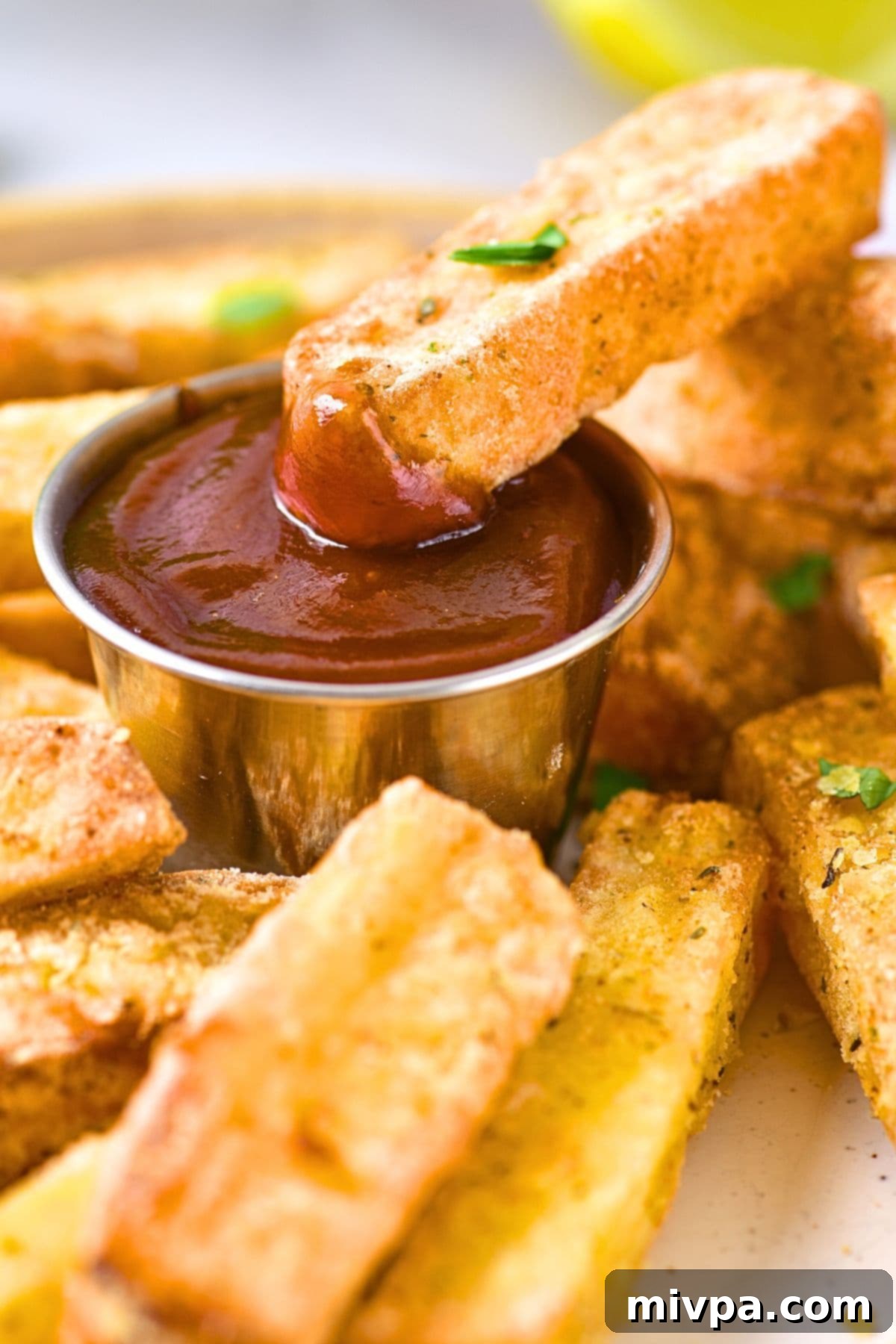 A halloumi fry being dipped into a small bowl of ketchup, with more crispy fries on a plate in the background.