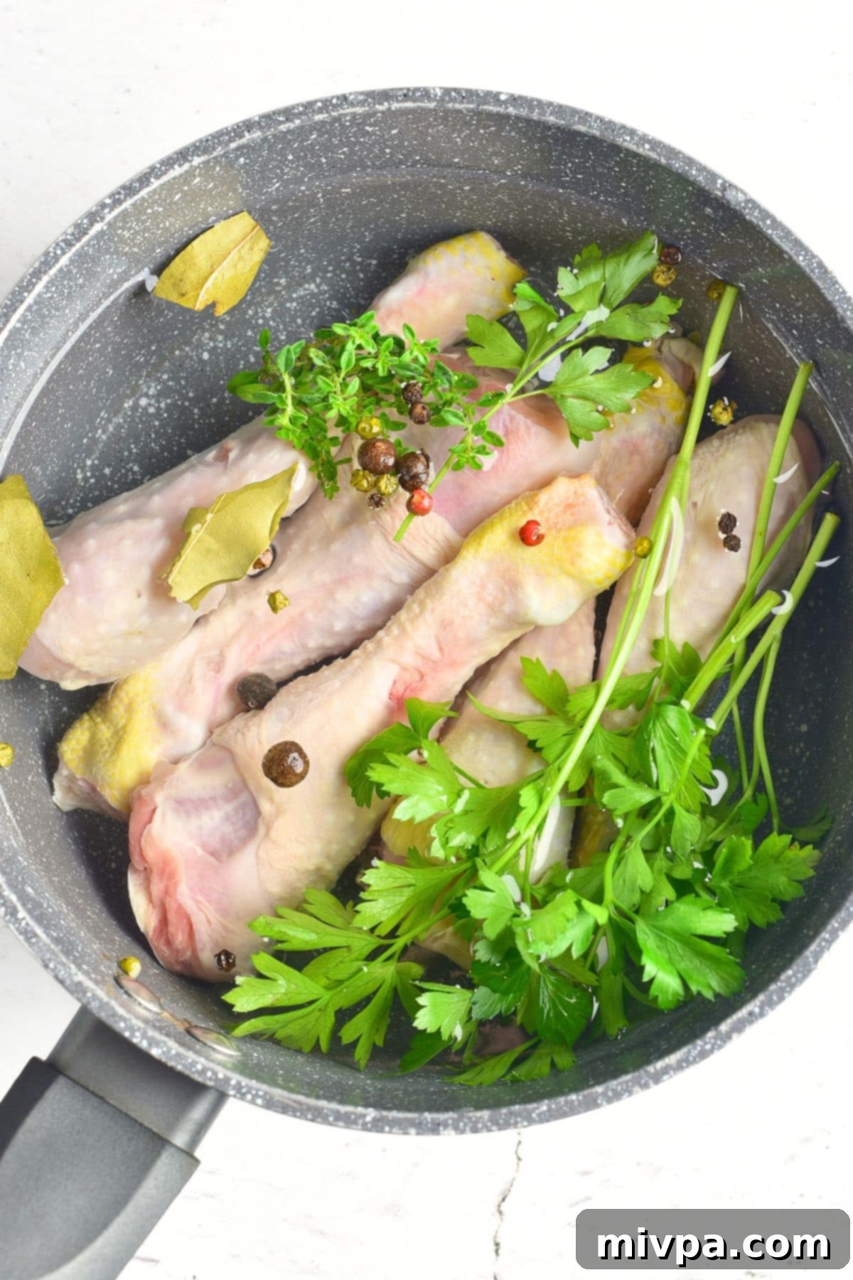 A pot with chicken drumsticks, fresh parsley, thyme, peppercorns, and bay leaves in water.