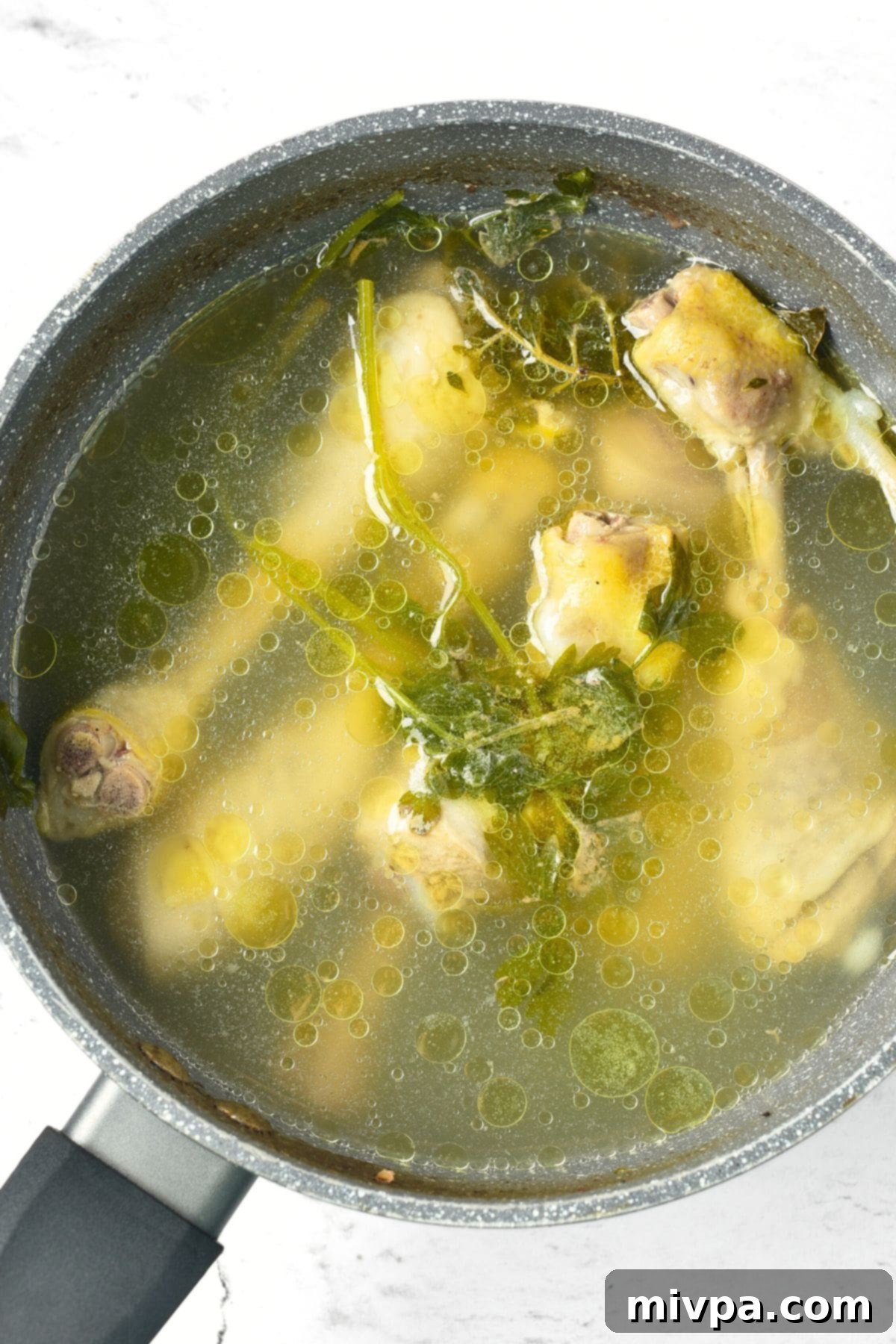 Homemade chicken broth and chicken drumsticks in a pot.