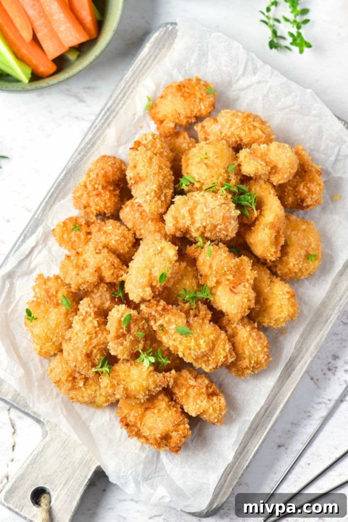 Homemade Gluten-Free Chicken Nuggets Top-down view of a rustic wooden board piled with homemade gluten-free chicken nuggets, ready to be served.