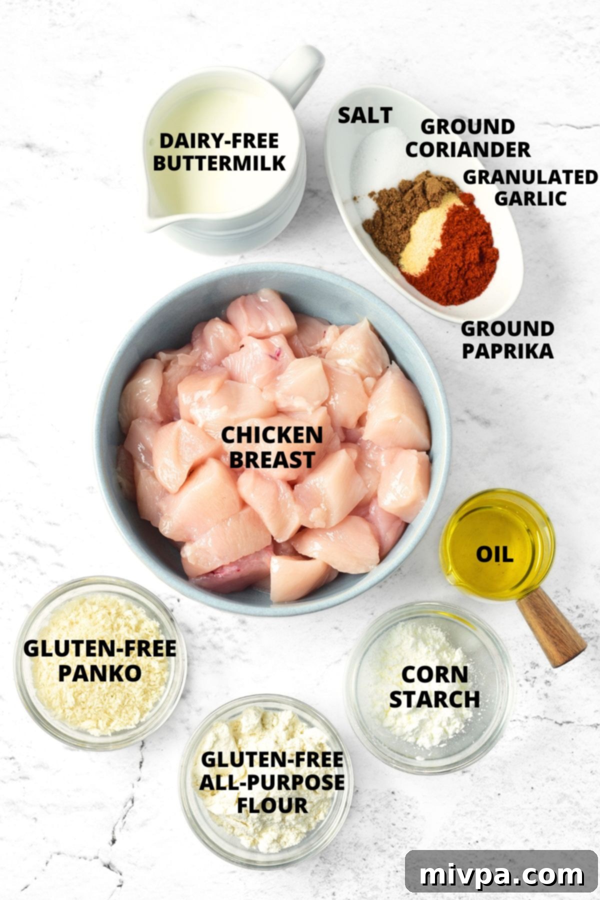 Gluten-Free Chicken Nuggets Recipe (Dairy-Free) All ingredients for the gluten-free chicken nuggets recipe neatly laid out on a clean marble board, including chicken, flours, spices, buttermilk, panko, and oil.