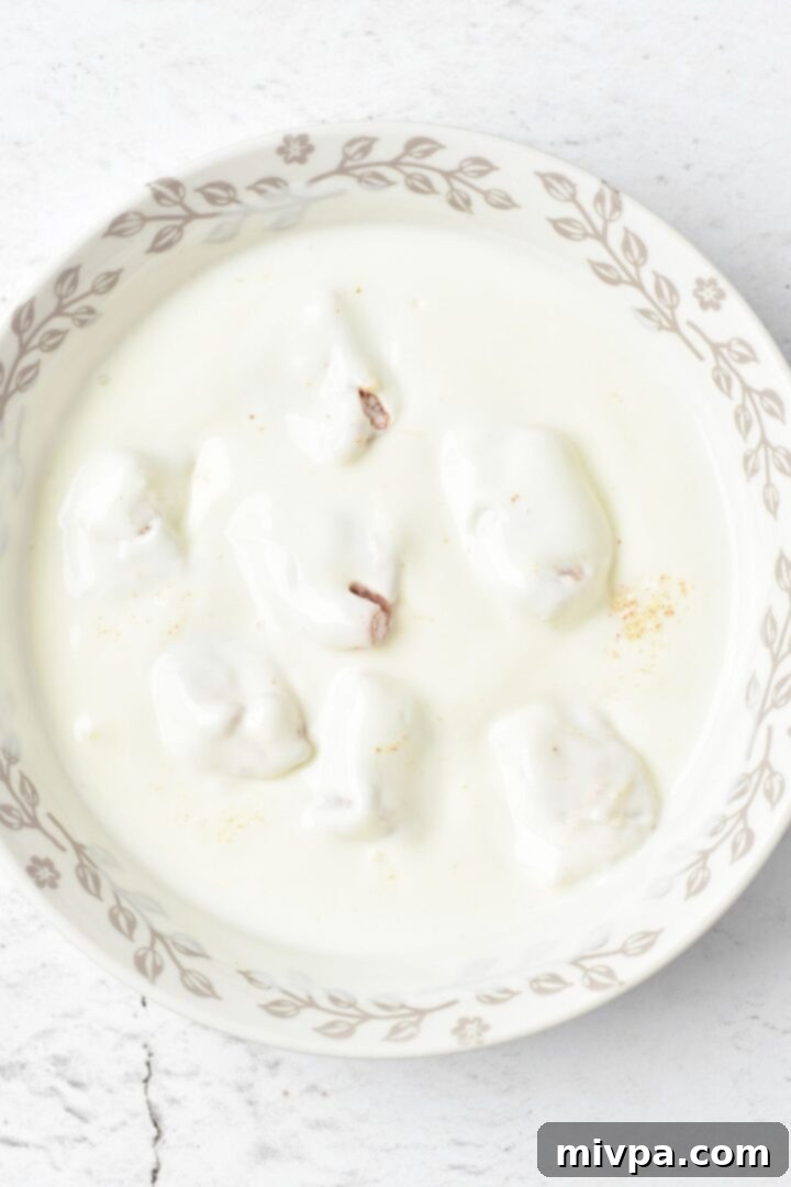 Homemade Chicken Nuggets (Gluten-Free, Dairy-Free) A hand dredging chicken cubes into a bowl of dairy-free buttermilk for coating.