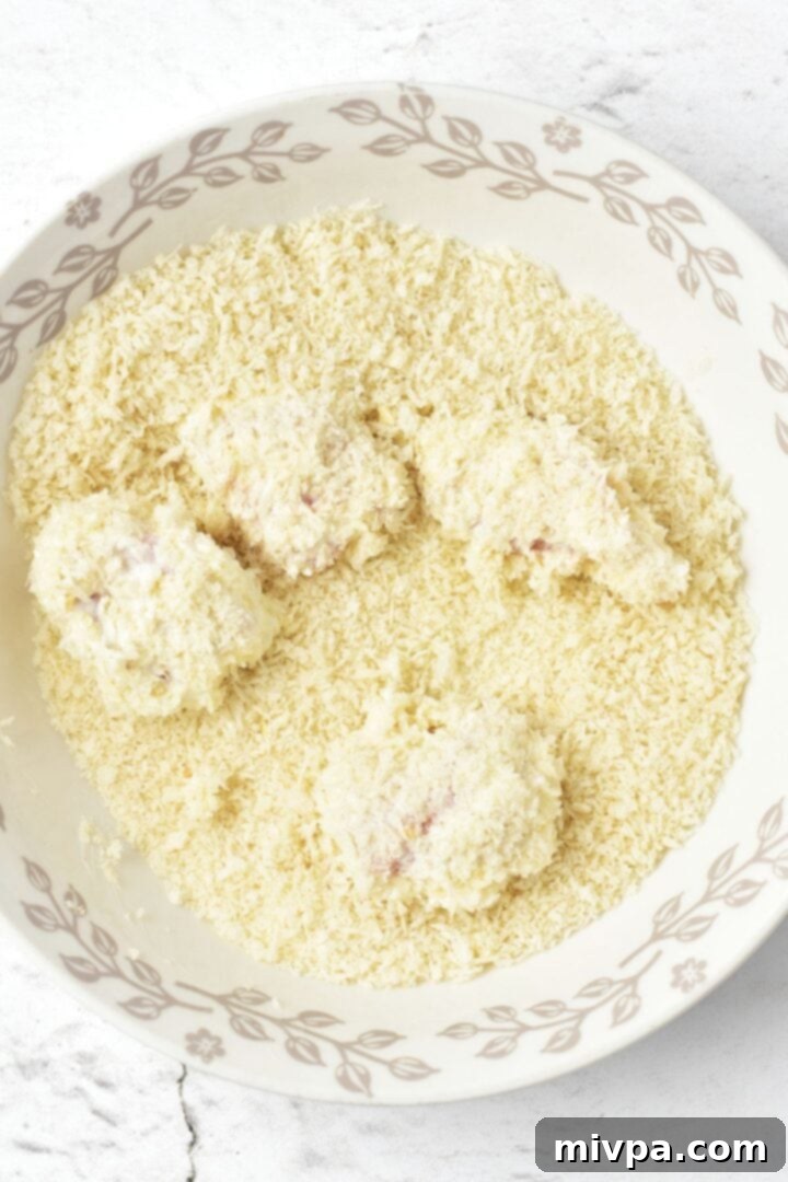 How to Make Gluten-Free Chicken Nuggets Chicken nugget being rolled and coated thoroughly in a bowl of gluten-free panko breadcrumbs.