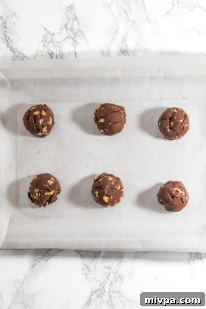 Chocolate Walnut Cookie Dough Balls Neatly arranged cookie dough balls on a parchment-lined baking sheet, ready for the oven.