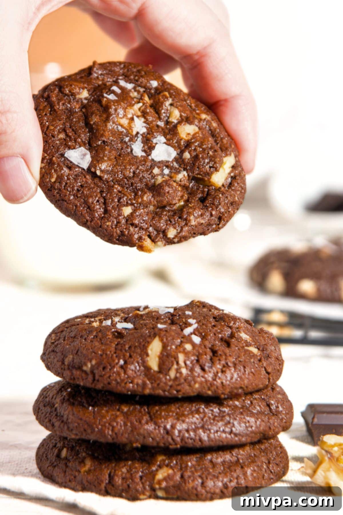 Gluten-Free Chocolate Walnut Cookie in Hand A hand gently lifting a chocolate walnut cookie from a delectable stack, highlighting its perfect form.