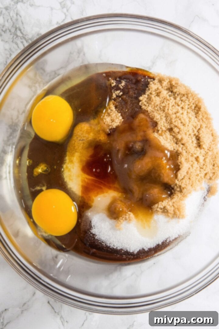 Wet Ingredients for Fudgy Walnut Chocolate Cookies Sugar, eggs, and vanilla blended into the rich chocolate mixture in a glass bowl, creating a smooth wet base.