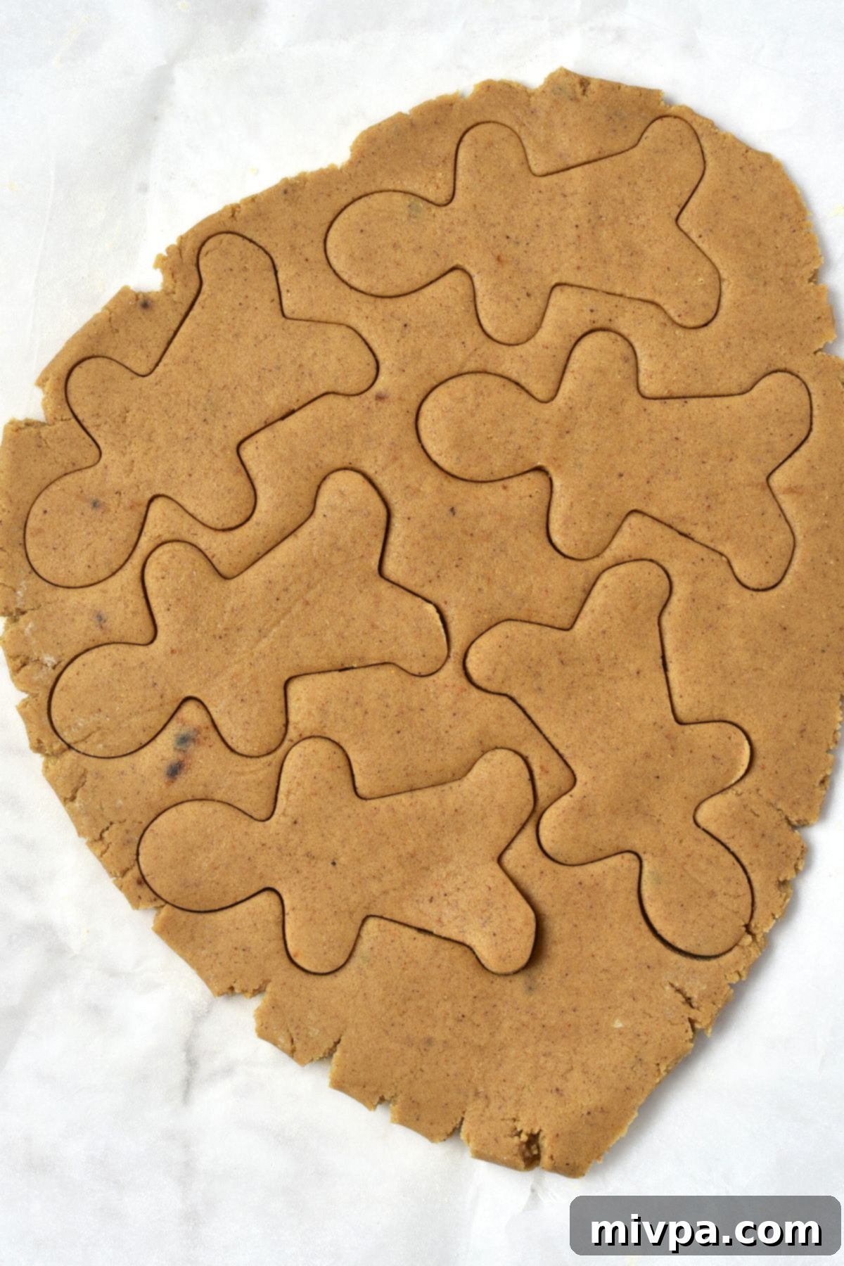 Easy Gluten-Free Gingerbread Men Cookie Recipe (Dairy-Free) Cutting out cookie dough with a gingerbread man cutter, showing the process of shaping cookies.