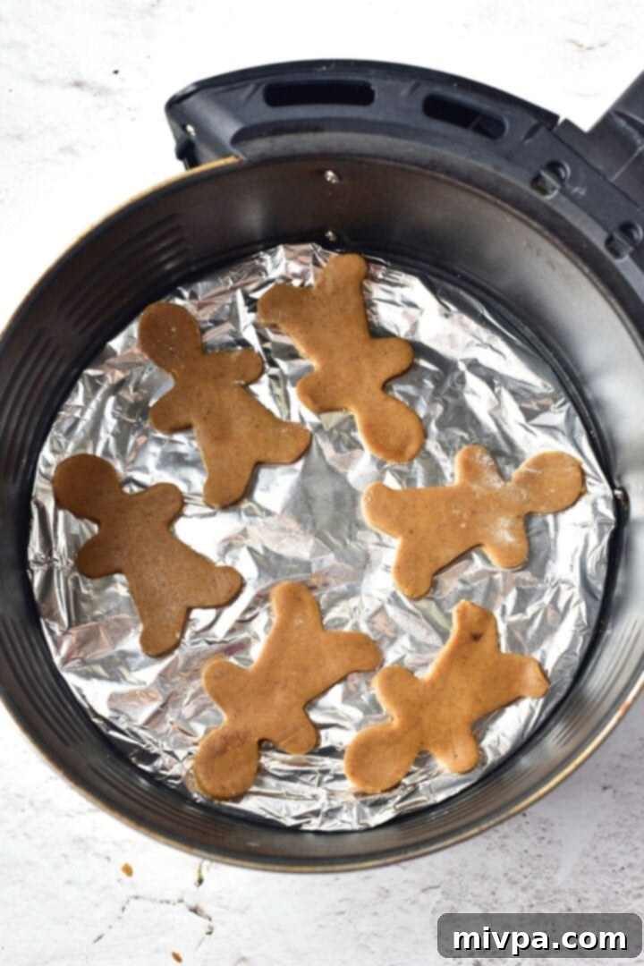 Easy Gluten-Free Gingerbread Men (Dairy-Free) Cookie dough cutouts on aluminum foil in air fryer basket, ready to cook.