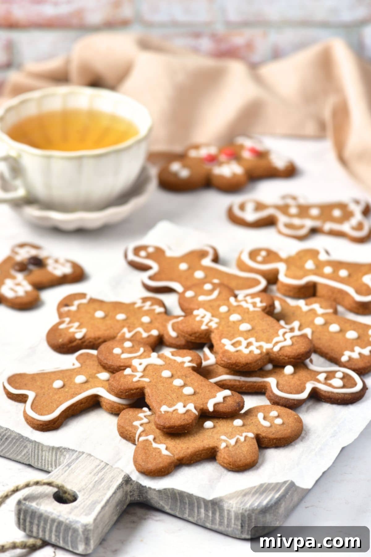 GF DF Gingebread Men Cookies Gingebread cookies on wooden board with cup of tea in the background, creating a cozy festive scene.
