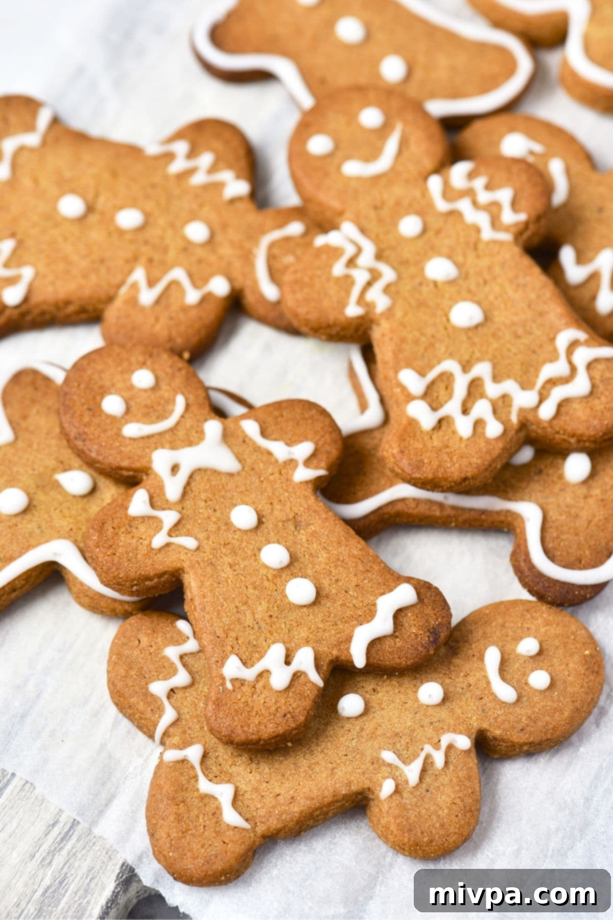 Delicious Gluten-Free Dairy-Free Gingerbread Men 2 Gluten-free dairy-free gingerbread men cookies on parchment-lined wooden board, beautifully decorated.