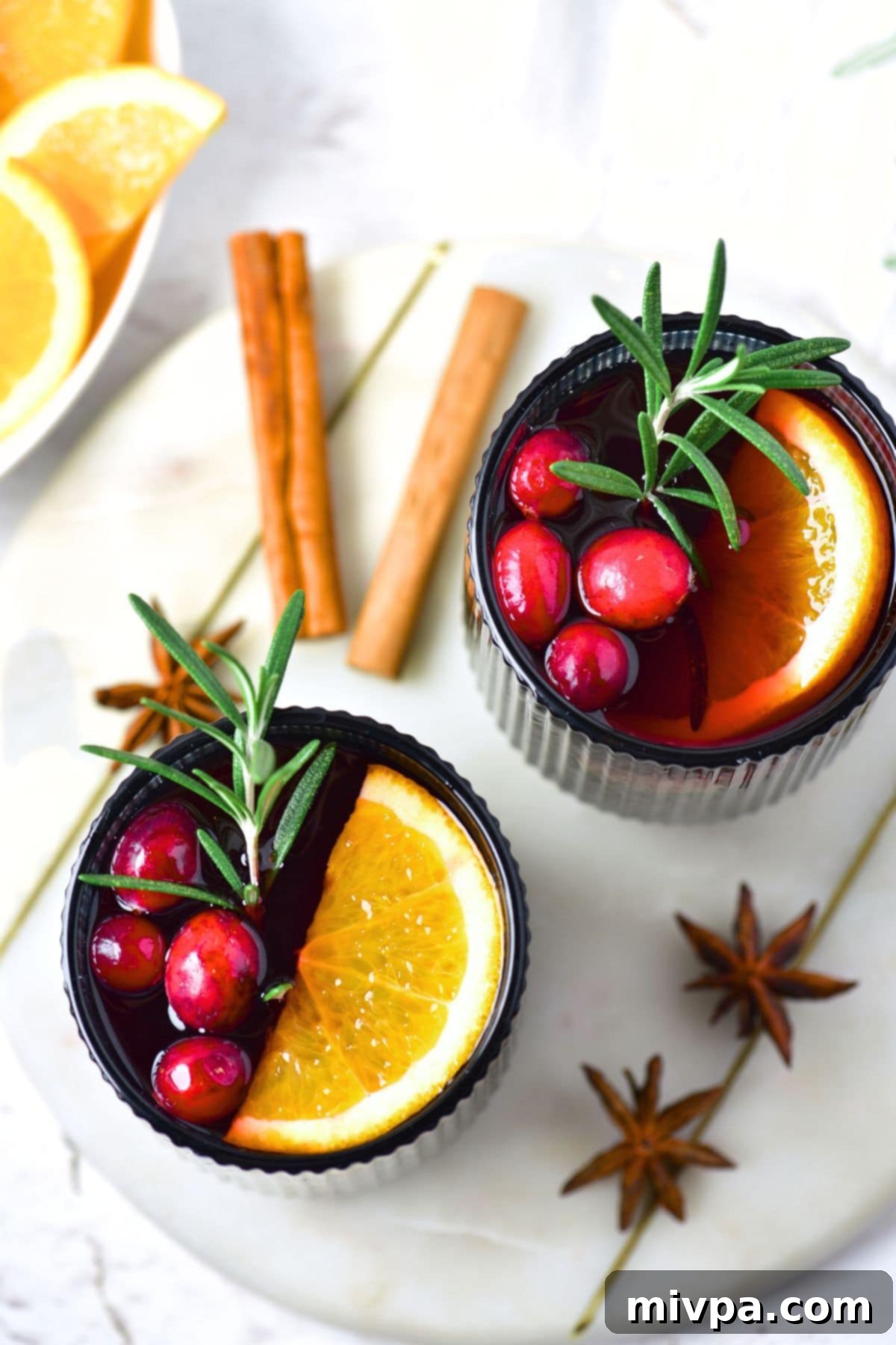 Simple Homemade Mulled Wine Gluten-Free and Vegan 2 A glass of homemade mulled wine garnished with orange slices, cranberries, and a sprig of rosemary, set against a cozy background.