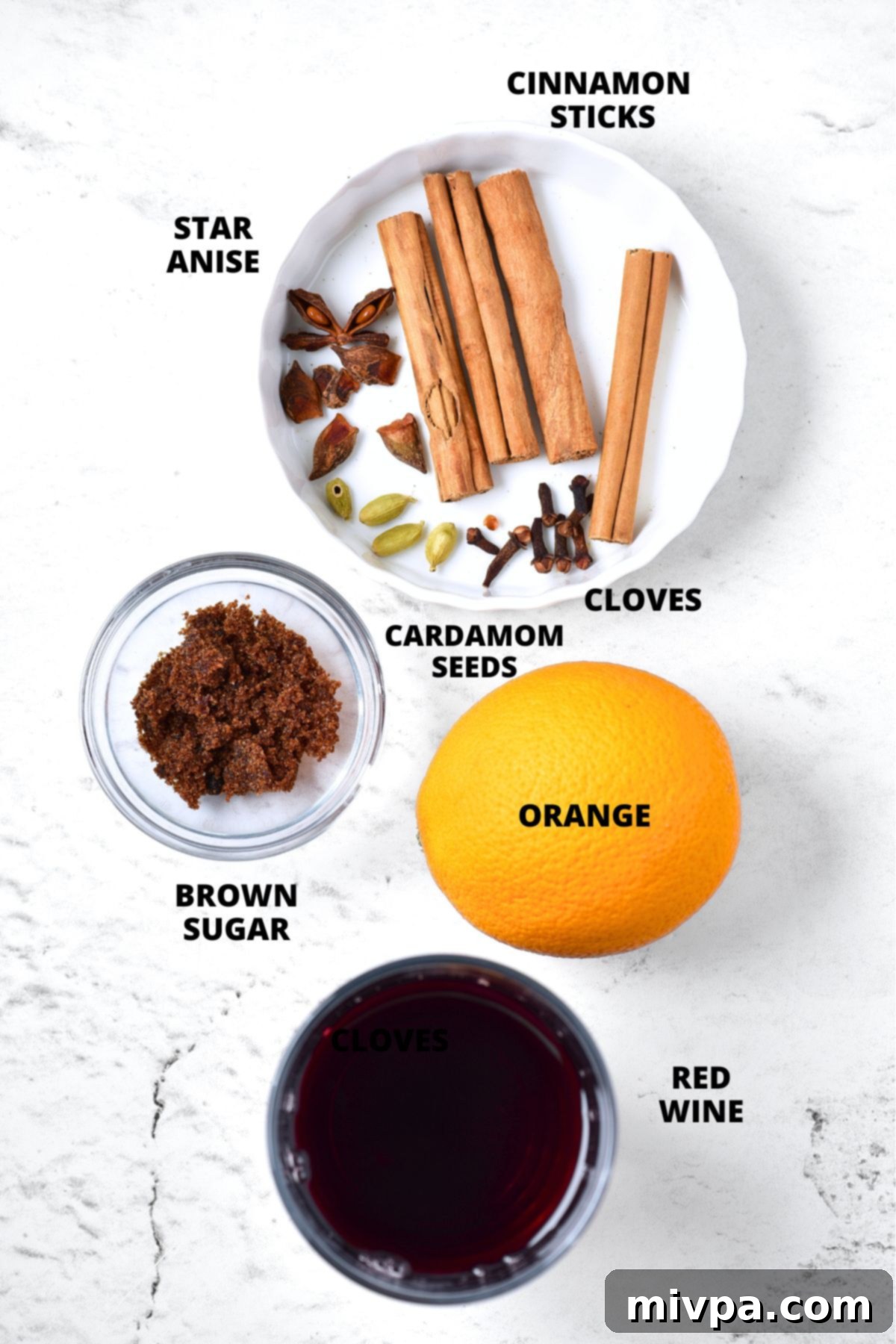 Simple Homemade Mulled Wine Gluten-Free and Vegan 5 A flat lay of all the ingredients needed for mulled wine, including a bottle of red wine, an orange, brown sugar, cinnamon sticks, star anise, cardamom pods, and cloves.