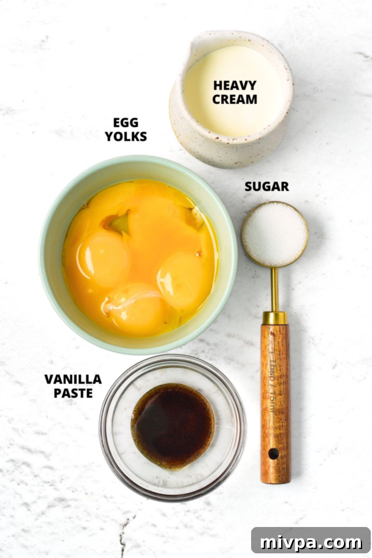 A flat lay image displaying the simple ingredients for crème brûlée: heavy cream, egg yolks, granulated sugar, and vanilla paste, laid out on a kitchen counter.