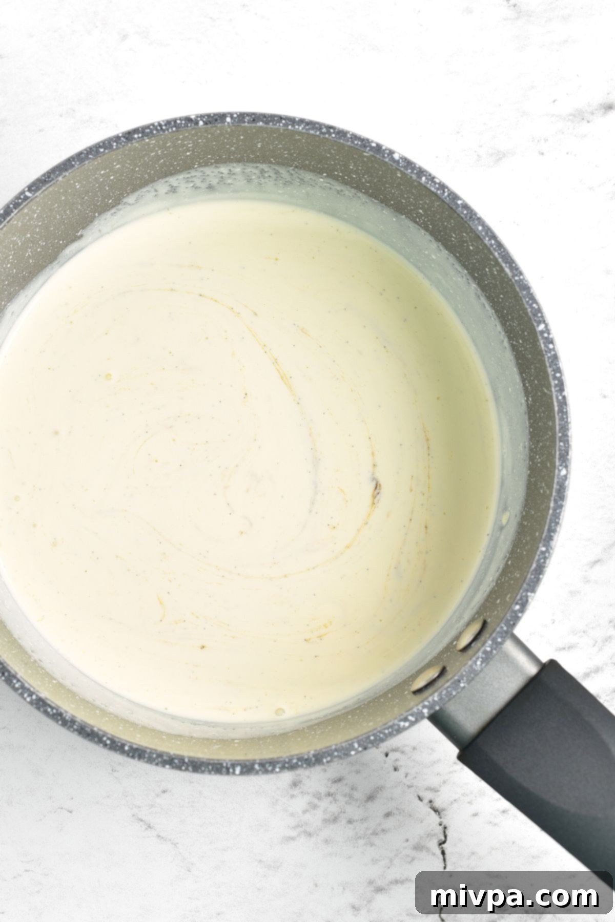 Heavy cream and vanilla bean paste heating gently in a saucepan on the stove, infusing flavor for the crème brûlée custard.
