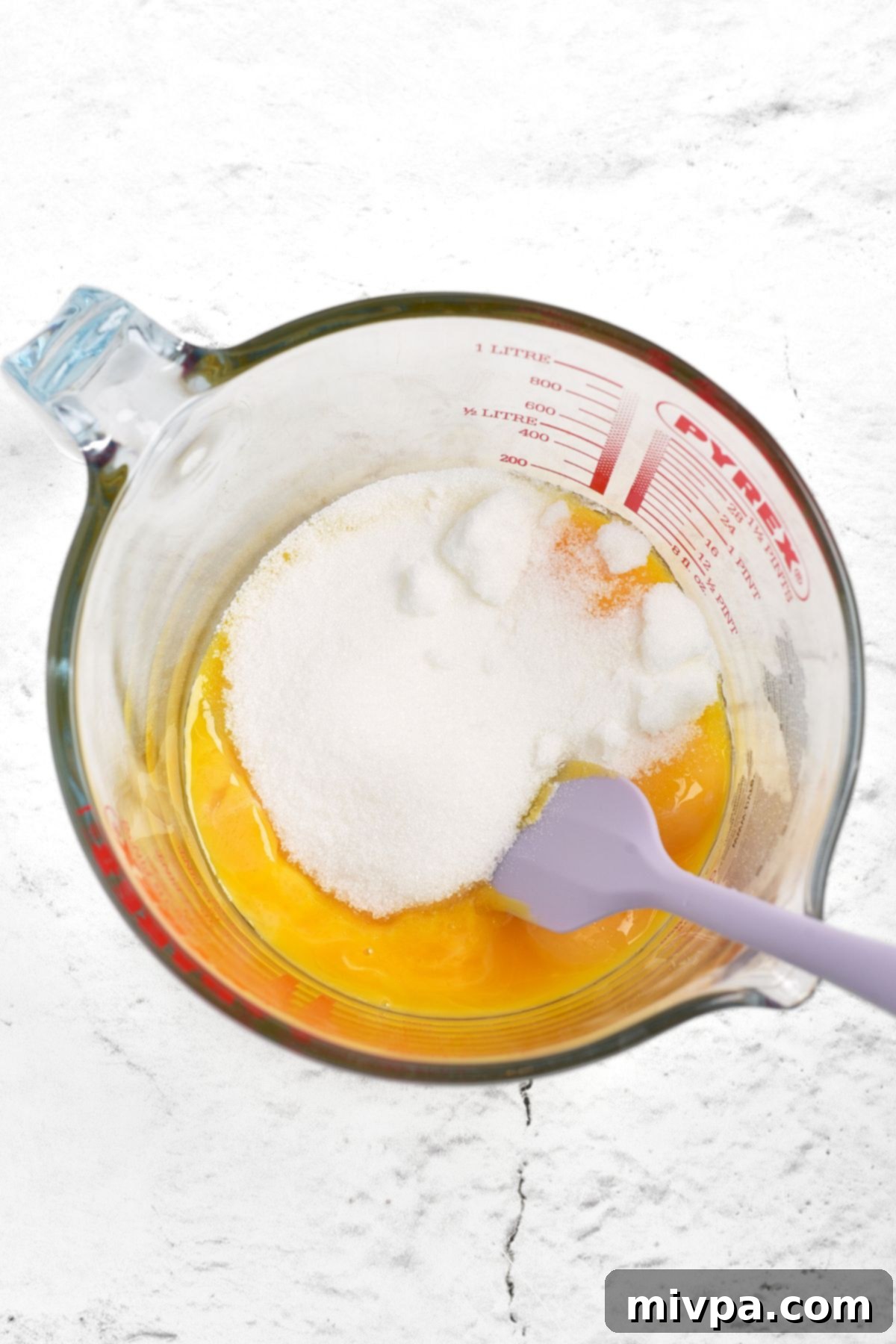 Egg yolks and sugar being whisked together in a mixing bowl until light, pale yellow, and fluffy.