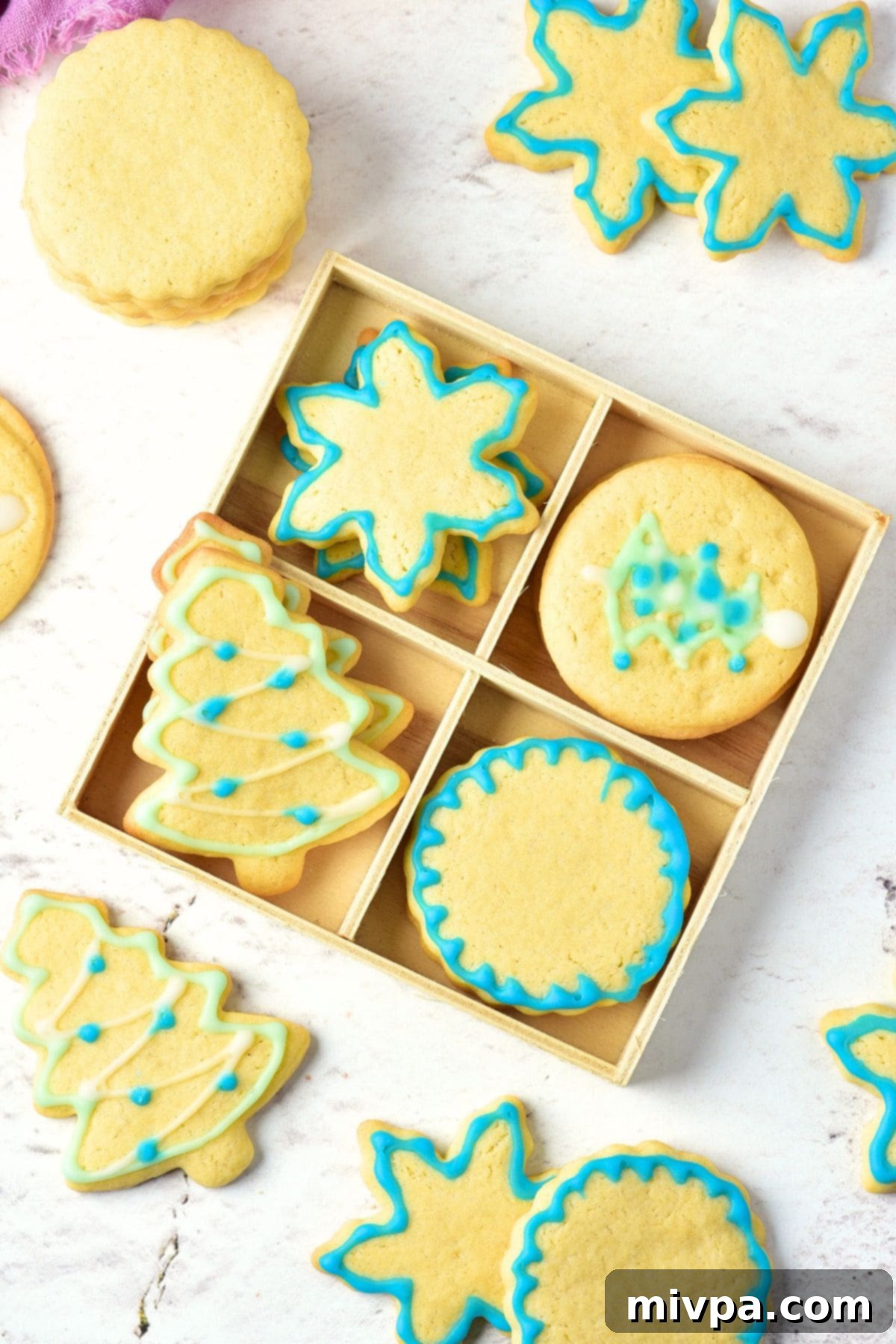 Top down view of a box of gluten-free Christmas sugar cookies, artfully decorated with festive icing in red, green, and white. Some cookies are star-shaped, others resemble Christmas trees or snowflakes, all nestled in a rustic wooden box.