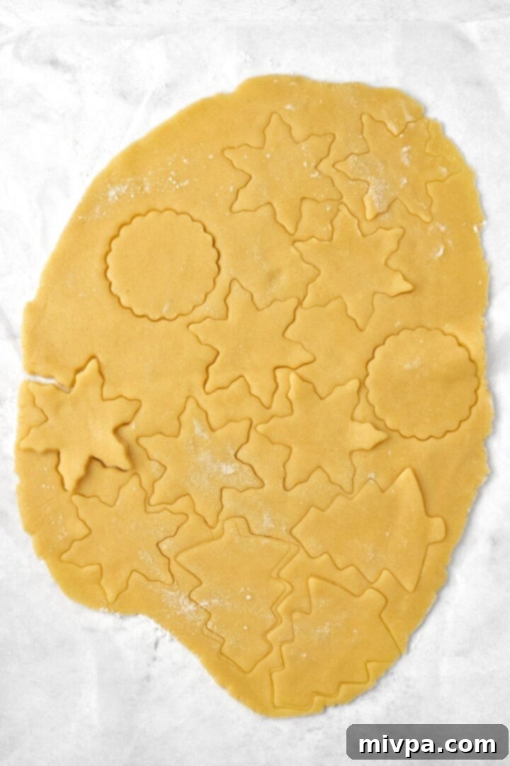 Various festive shapes, including stars and Christmas trees, neatly cut from the cookie dough and arranged on parchment paper, ready to be transferred to a baking sheet.