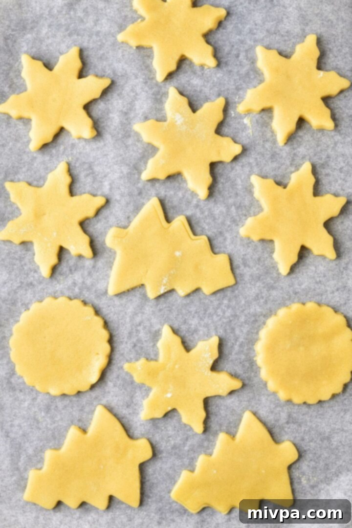 Neatly arranged raw cookie dough cut into star and Christmas tree shapes, placed on parchment paper on a baking sheet, ready for the oven.