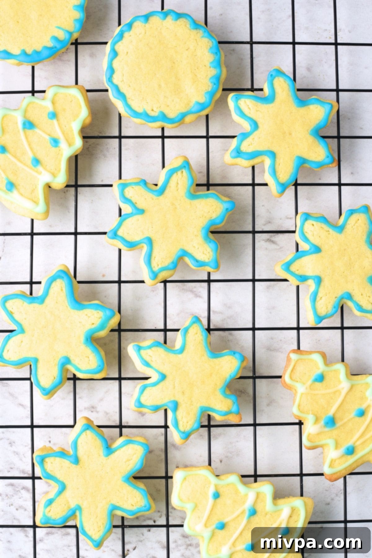 A wire rack filled with freshly decorated gluten-free dairy-free Christmas sugar cookies, adorned with intricate blue, green, and white icing designs, showcasing a beautiful array of festive shapes.