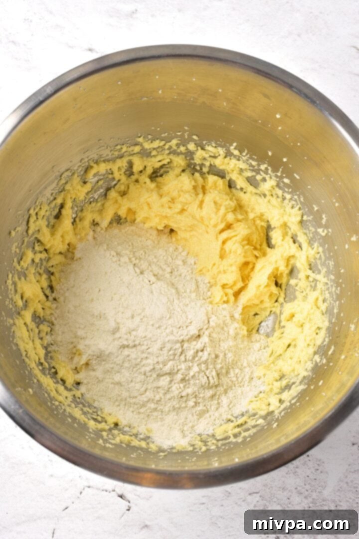 The white gluten-free flour mixture, baking powder, and salt are carefully added on top of the yellow wet dough mixture in a large mixing bowl, ready for combining.