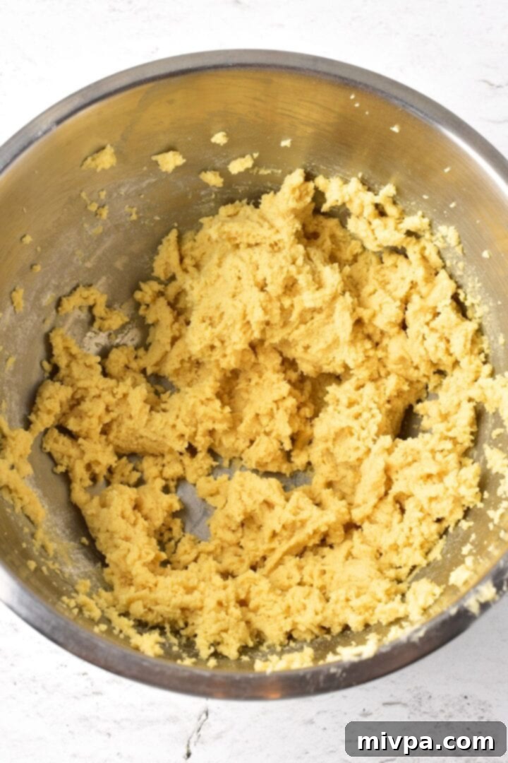 Smooth, yellow cookie dough neatly gathered into a ball inside a metal mixing bowl, waiting to be chilled.
