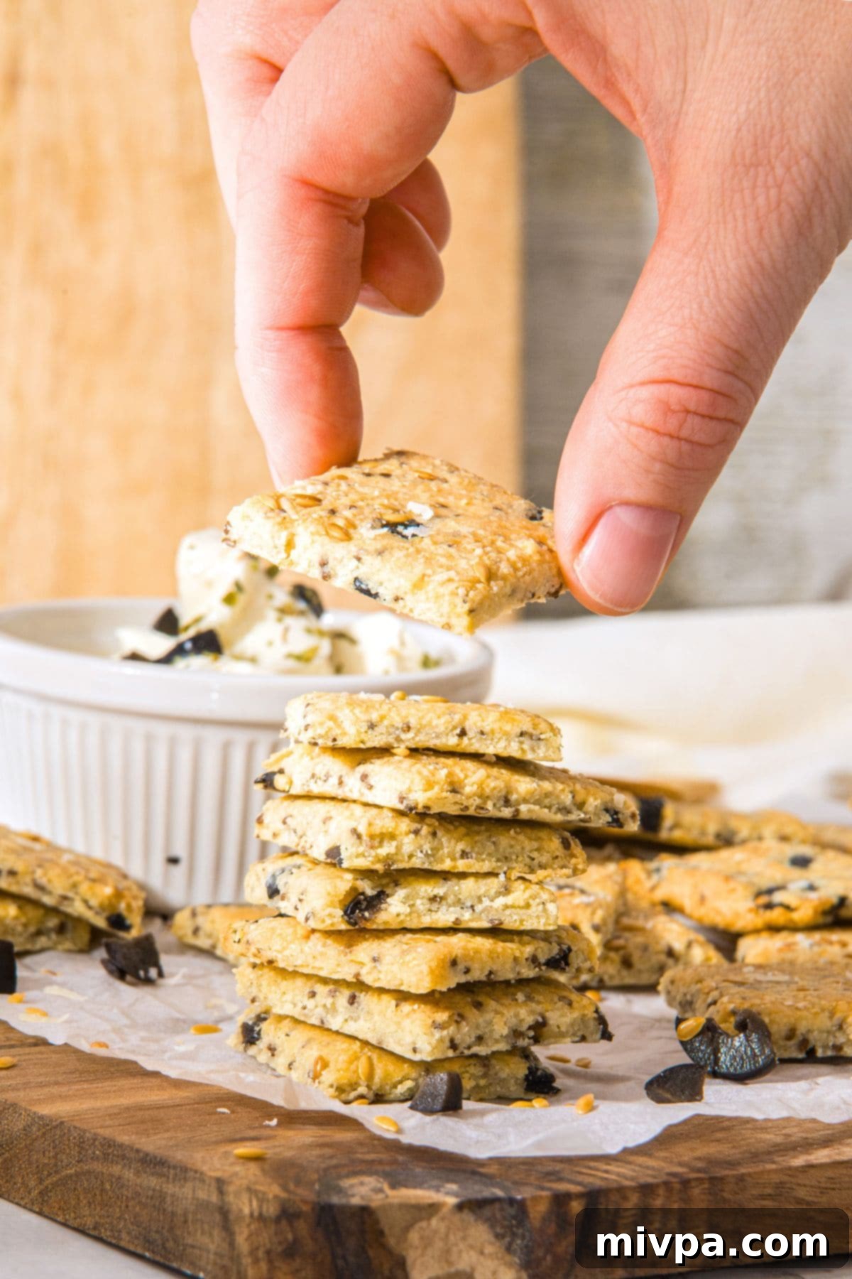 Low-Carb Almond Crackers (Gluten-Free, Dairy-Free) Hand holding up a cracker from a stack of gluten-free almond flour crackers