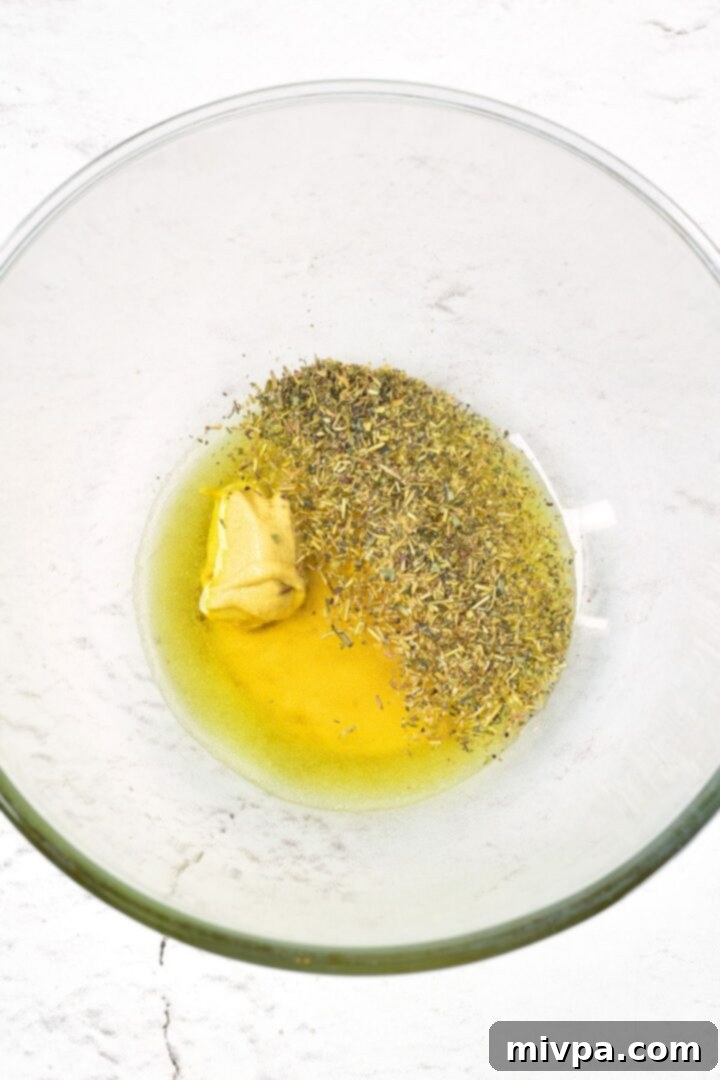 A glass bowl with mustard, honey, olive oil and dried herbs