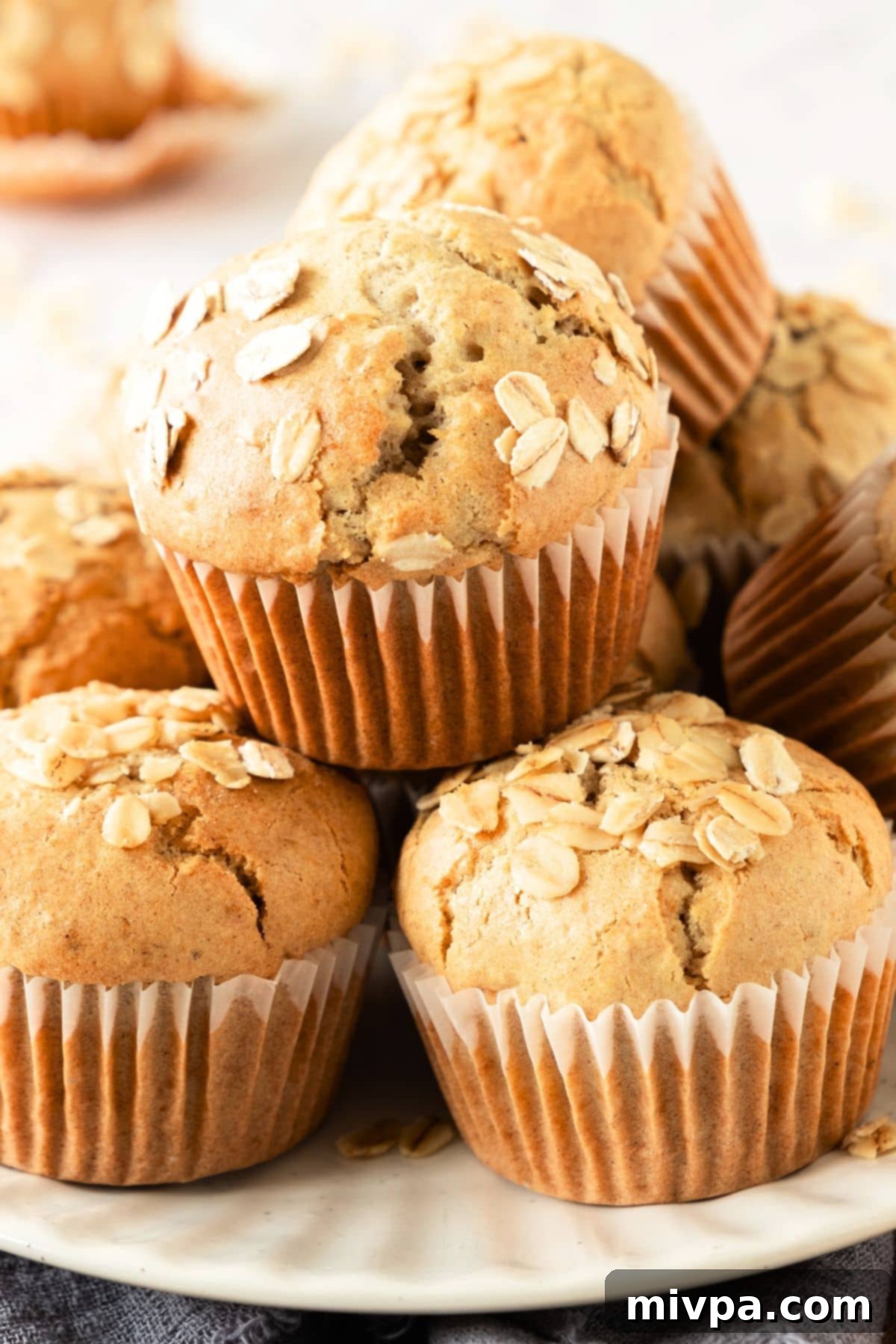 Gluten-Free Oatmeal Muffins (Dairy-Free) Up close view of a stack of golden-brown gluten-free oatmeal muffins, showcasing their soft, textured tops.