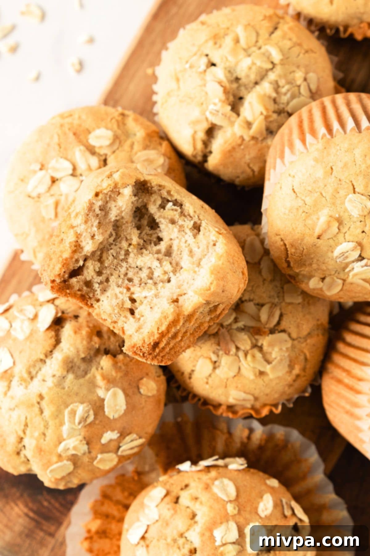 Easy Oatmeal Muffins (Gluten-Free, Dairy-Free) A half-eaten gluten-free oatmeal muffin resting on top of other freshly baked muffins.