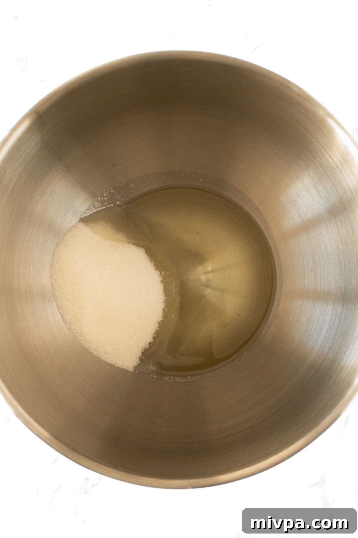 Gluten-Free Oatmeal Muffins (Dairy-Free) Sunflower oil and granulated sugar mixed in a metal bowl, forming a pale, combined mixture.