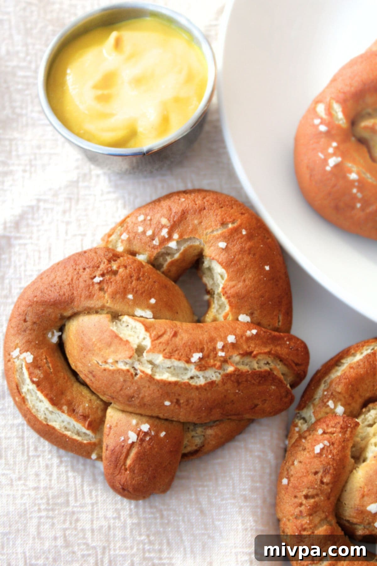 Top down view of gluten-free soft pretzels and mustard on tablecloth, ready to be served and enjoyed as a delicious snack or appetizer.
