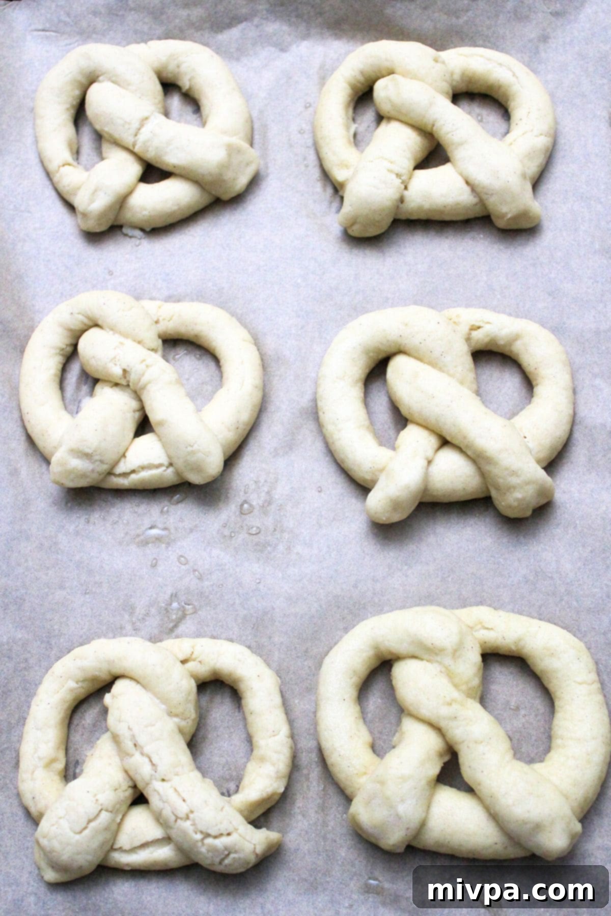 Gluten-free pretzel dough neatly arranged on parchment paper on a baking sheet, sprinkled with coarse sea salt, ready for the oven.