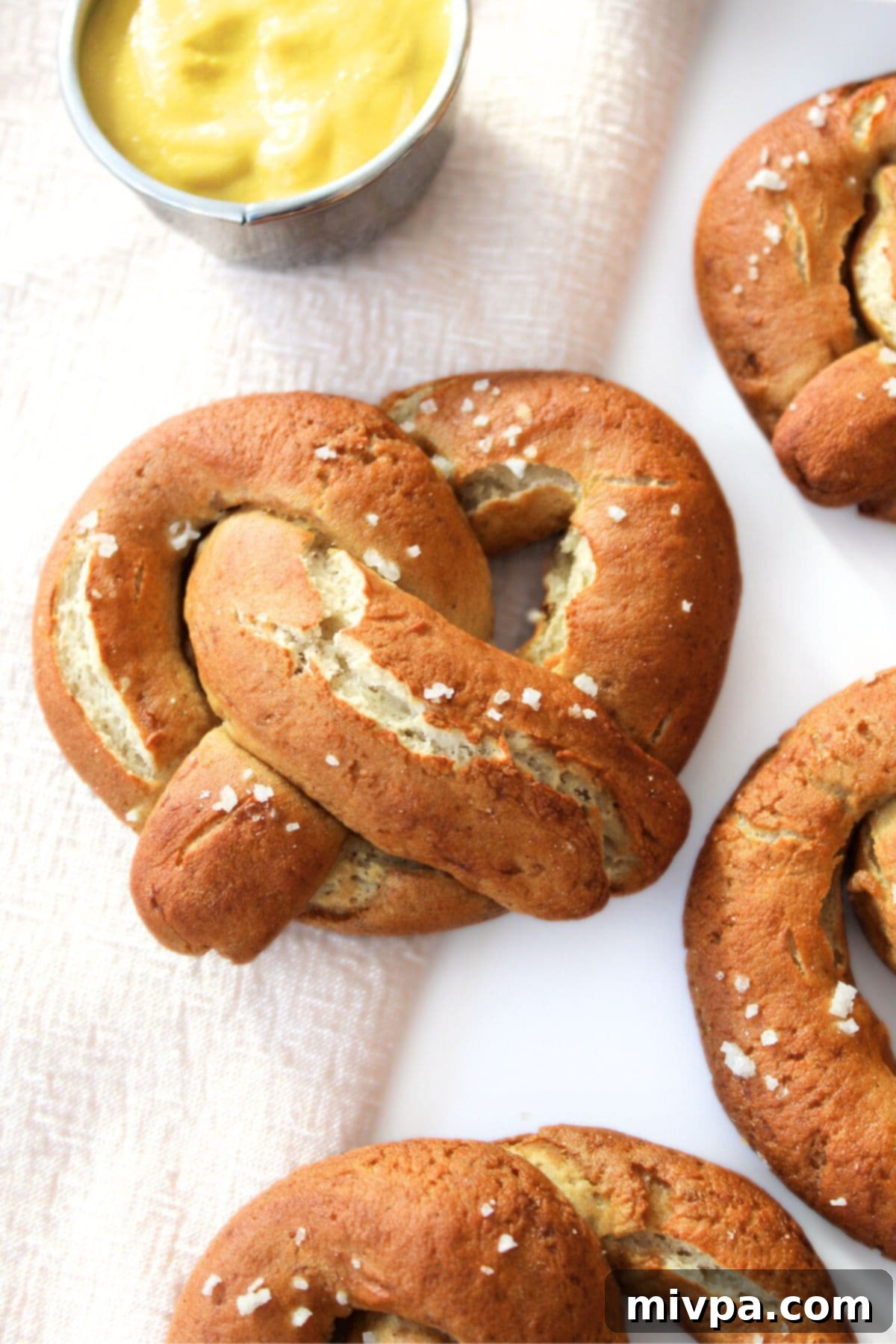 Gluten-free soft pretzels and mustard on a patterned tablecloth, presented as a delicious and appealing snack.