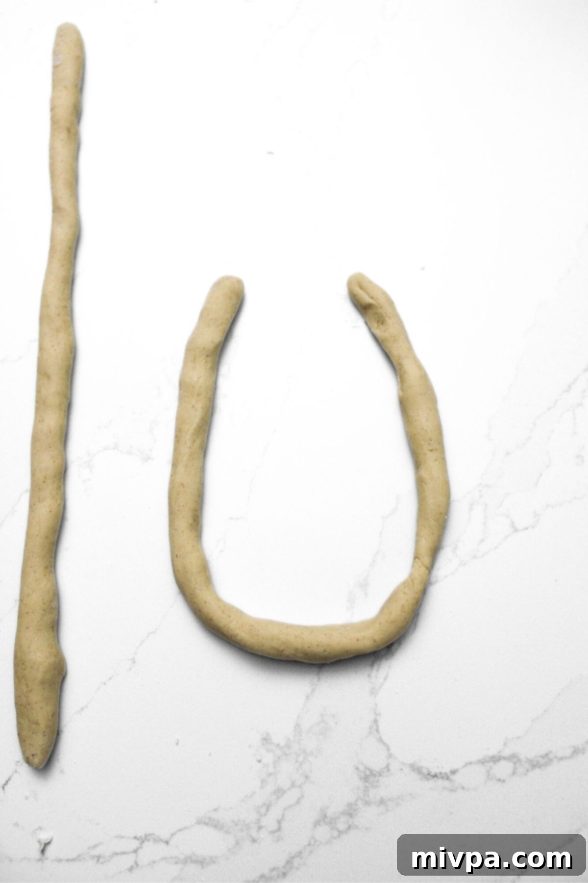 A portion of gluten-free pretzel dough skillfully rolled out into a long, thin rope on a lightly floured surface.