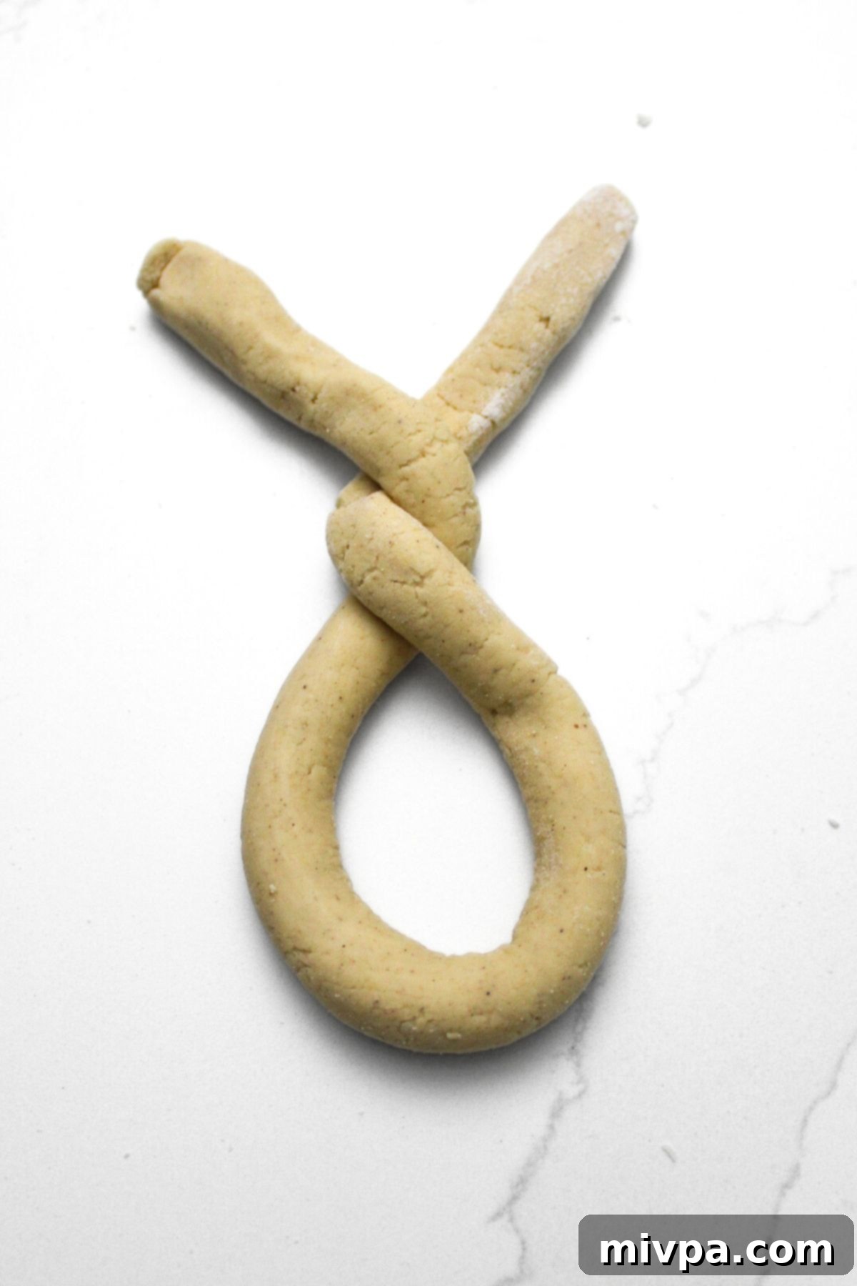 Pretzel dough shaped into a 'U' and then twisted twice, demonstrating an intermediate step in forming the classic pretzel shape.
