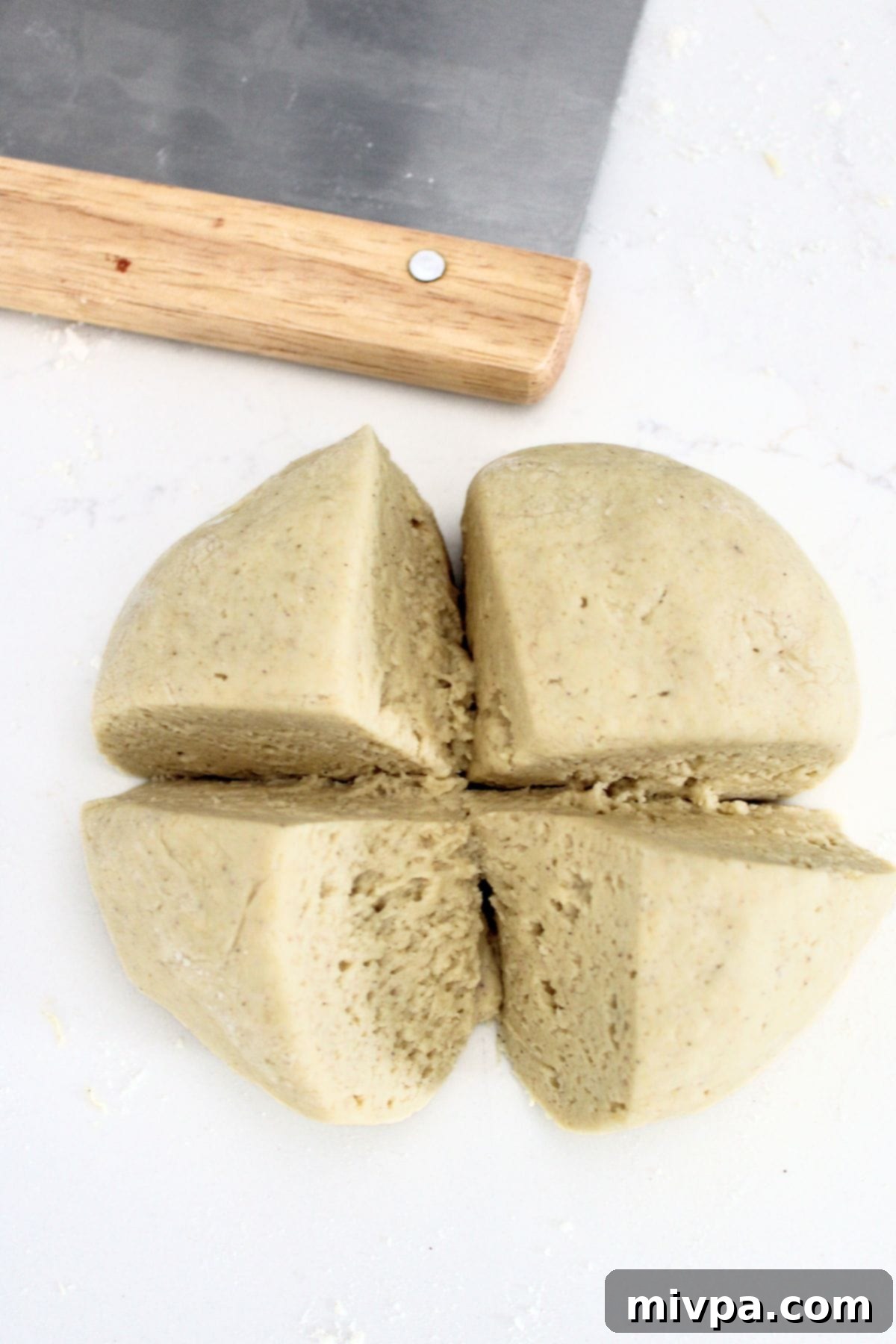 Cutting a ball of gluten-free pretzel dough into 4 pieces.