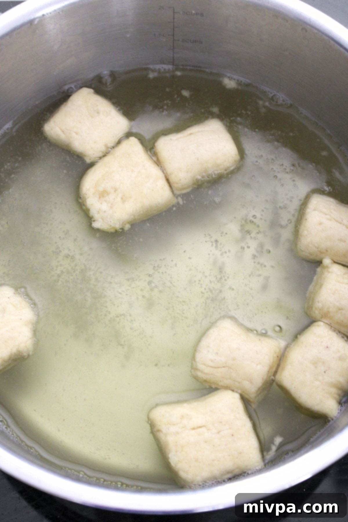 Boiling pieces of pretzel dough in a baking soda bath in a pot.
