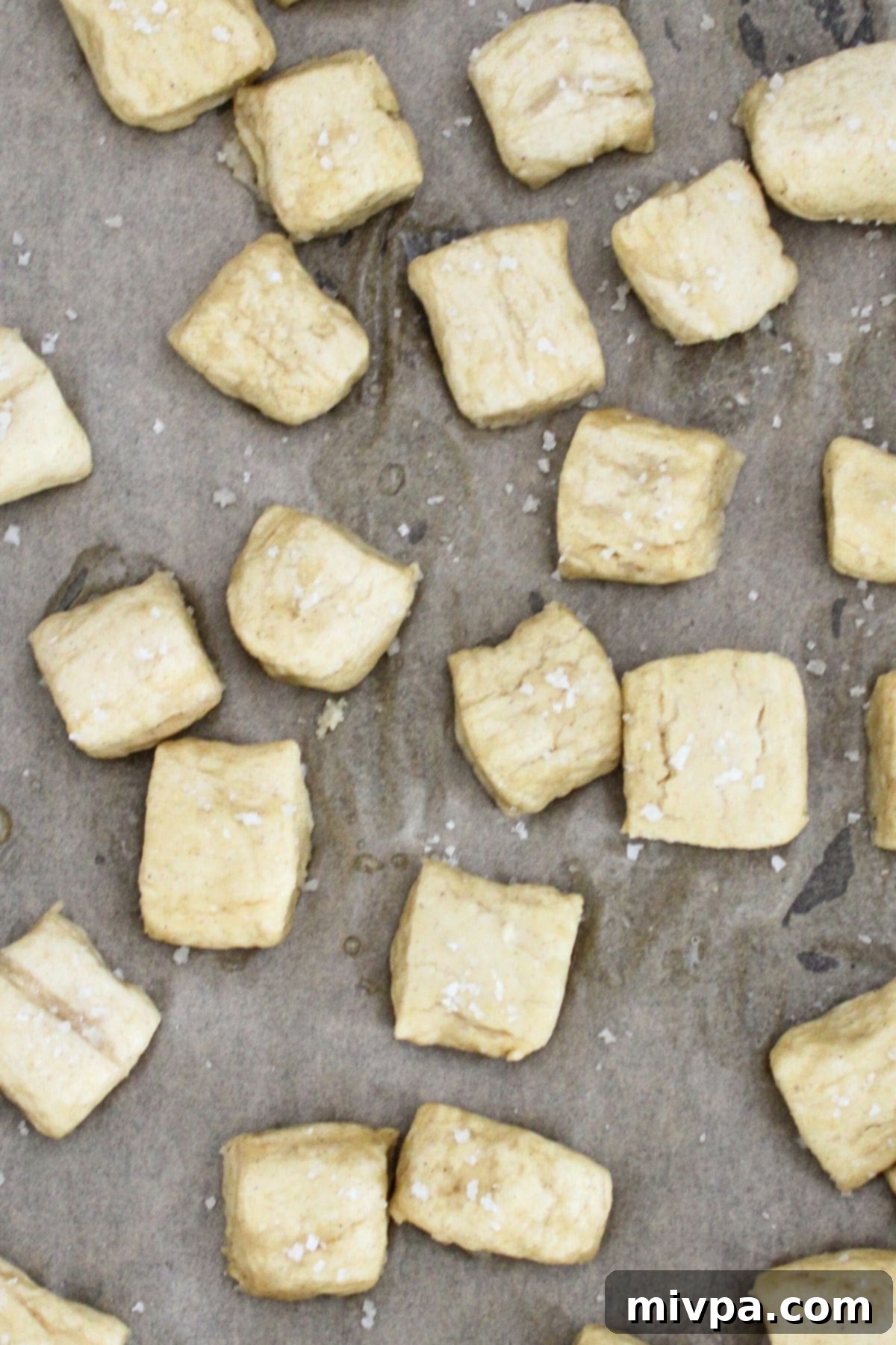 Boiled pretzel dough pieces arranged on parchment paper on a baking sheet.