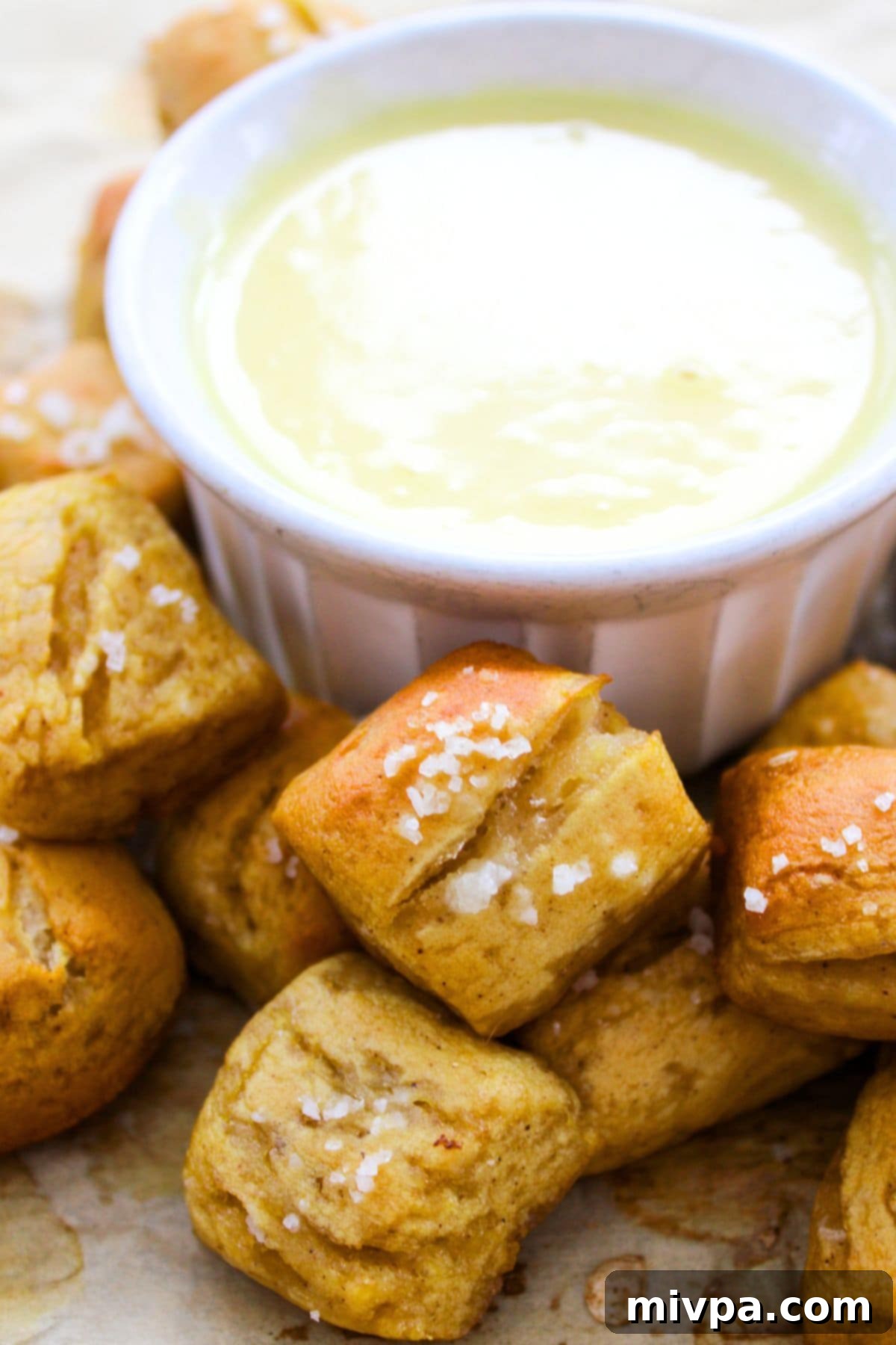 Pretzel bites and a bowl of cheese sauce on parchment paper, ready to serve.