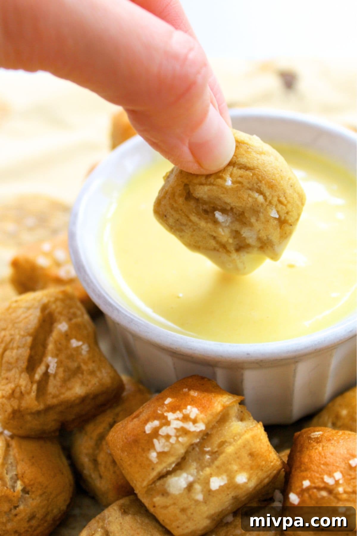 Dipping soft gluten-free pretzel bites into cheese sauce, a savory pairing.