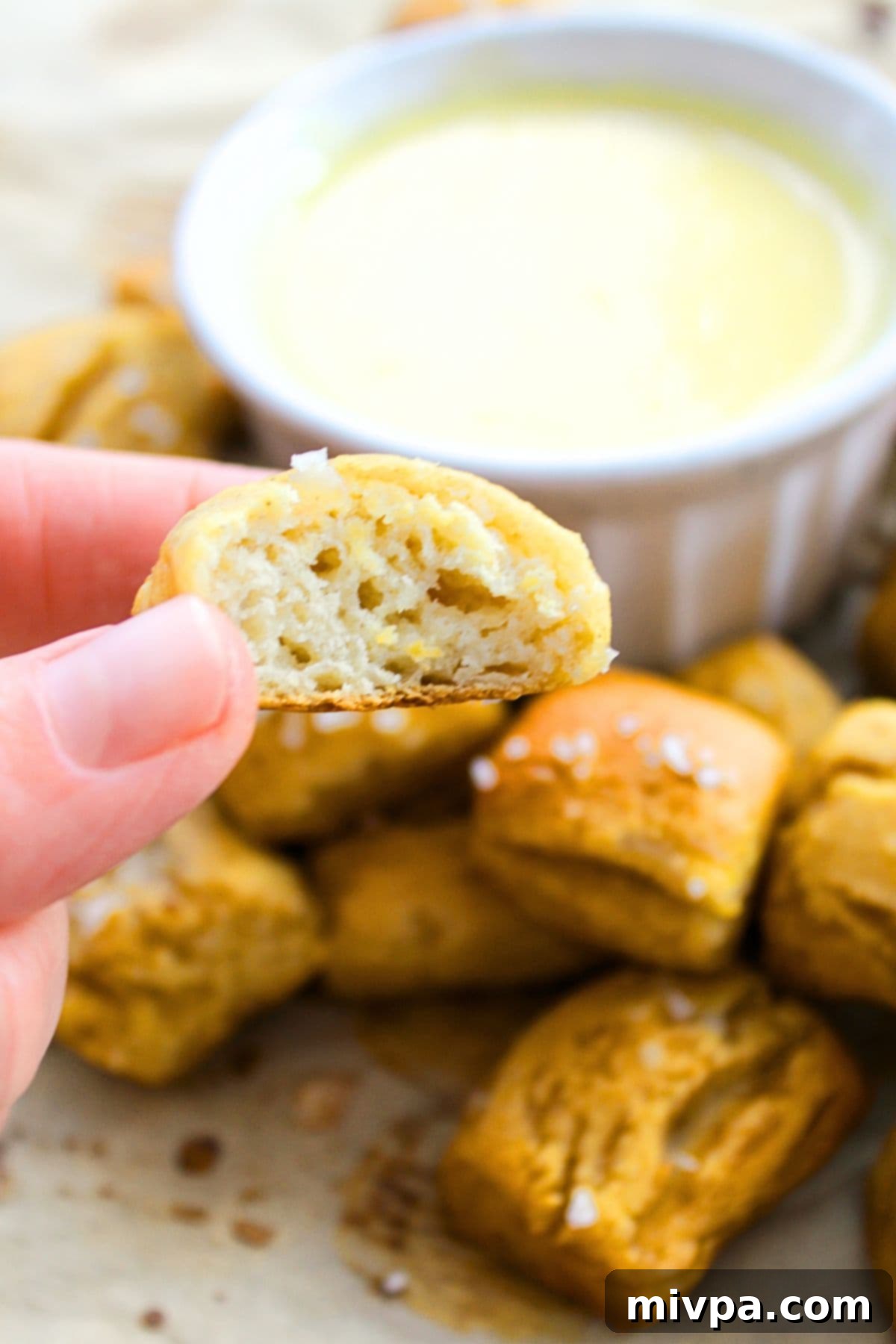 Holding up a half-eaten pretzel bite, showcasing its fluffy interior.