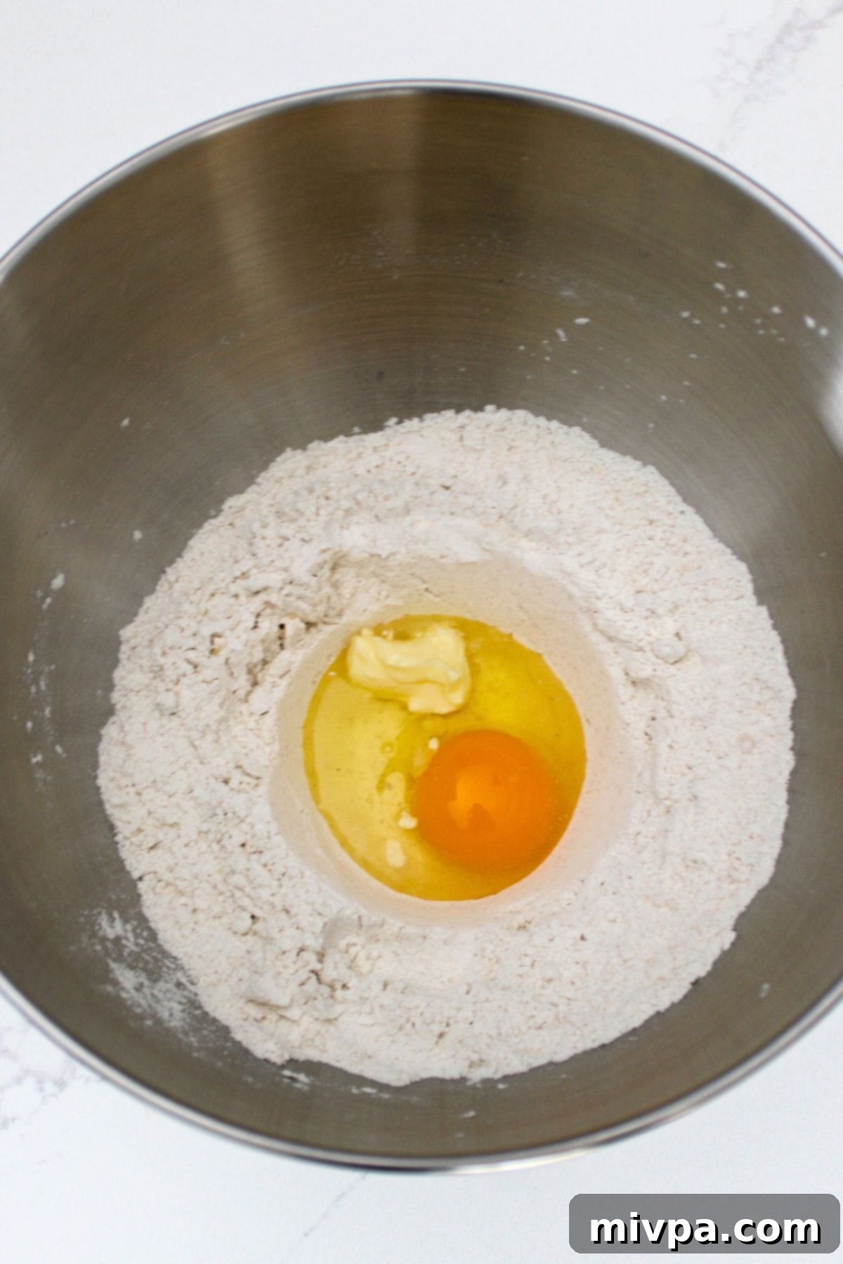 Flour, butter, and eggs are added to a metal mixing bowl.