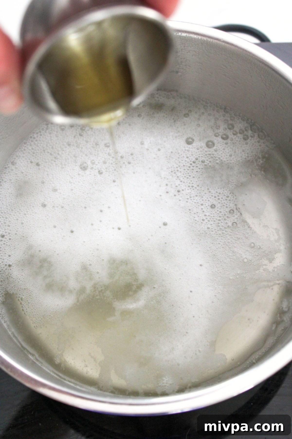 Pouring honey into a pot of boiling water for the baking soda bath.