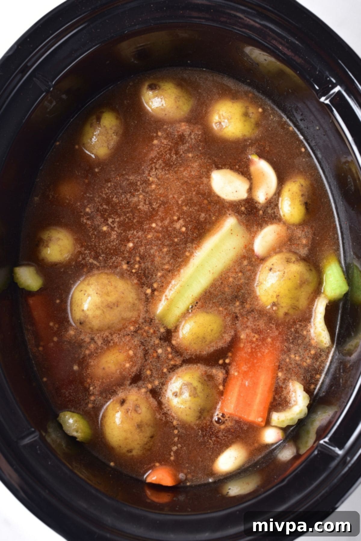 Vegetables, beef broth, and spices layered in a slow cooker before adding the brisket.