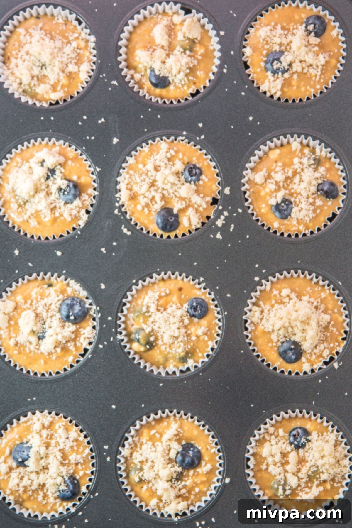 Easy Blueberry Cottage Cheese Muffins Muffin batter in a pan with the prepared streusel topping sprinkled generously over each cup.
